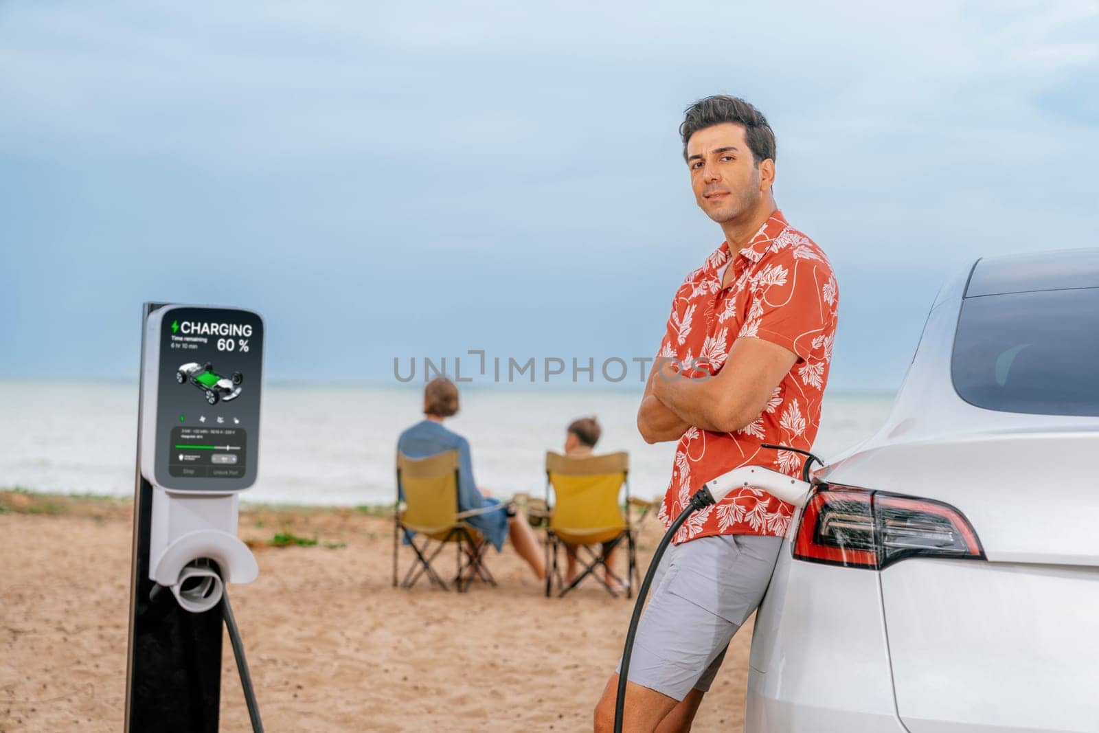 Family vacation trip traveling by the beach with electric car, dad or father recharge EV car while his family enjoy seascape beach. Family trip with alternative energy and eco-friendly car. Perpetual