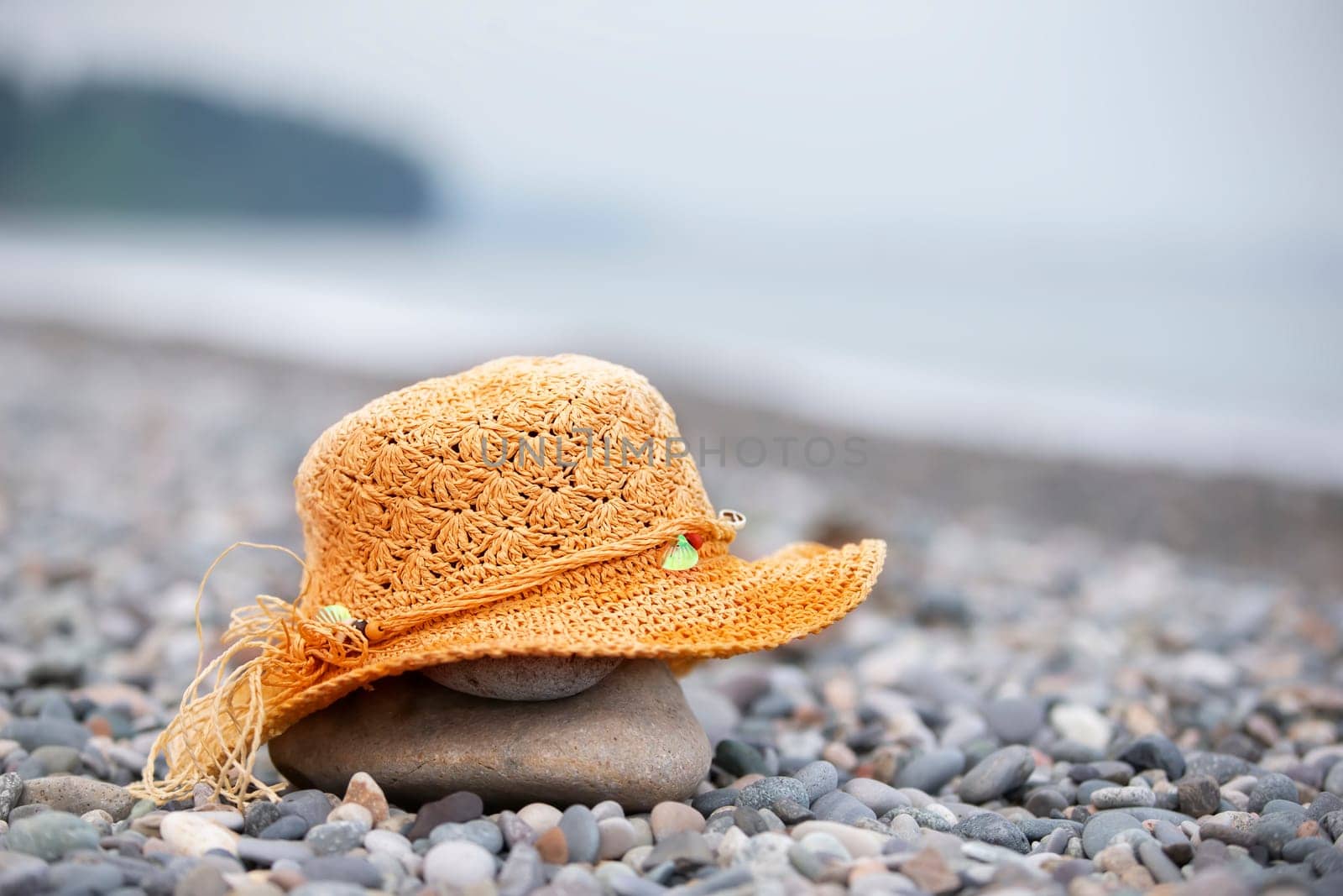 A straw beach hat lies on a pebble by the sea.