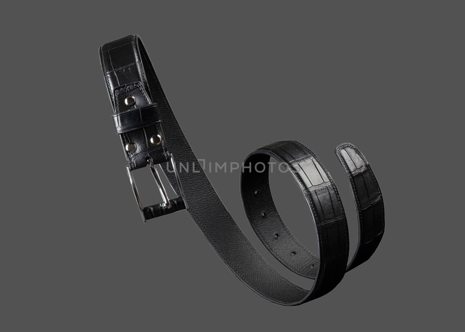 Black leather belt twisted in a spiral on a gray background. by Sviatlana