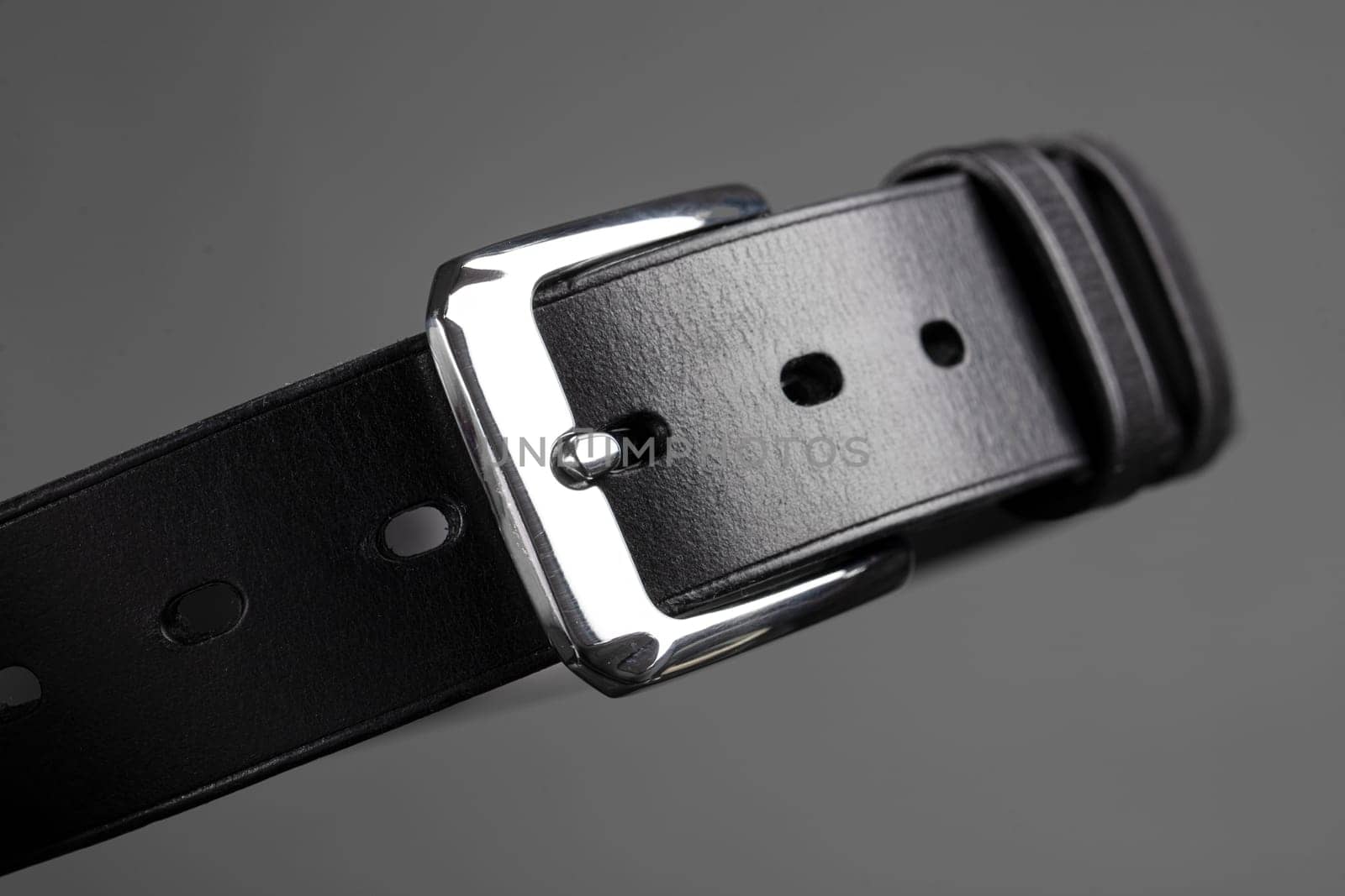 Part of a black leather belt with a metal buckle close-up on a gray background.