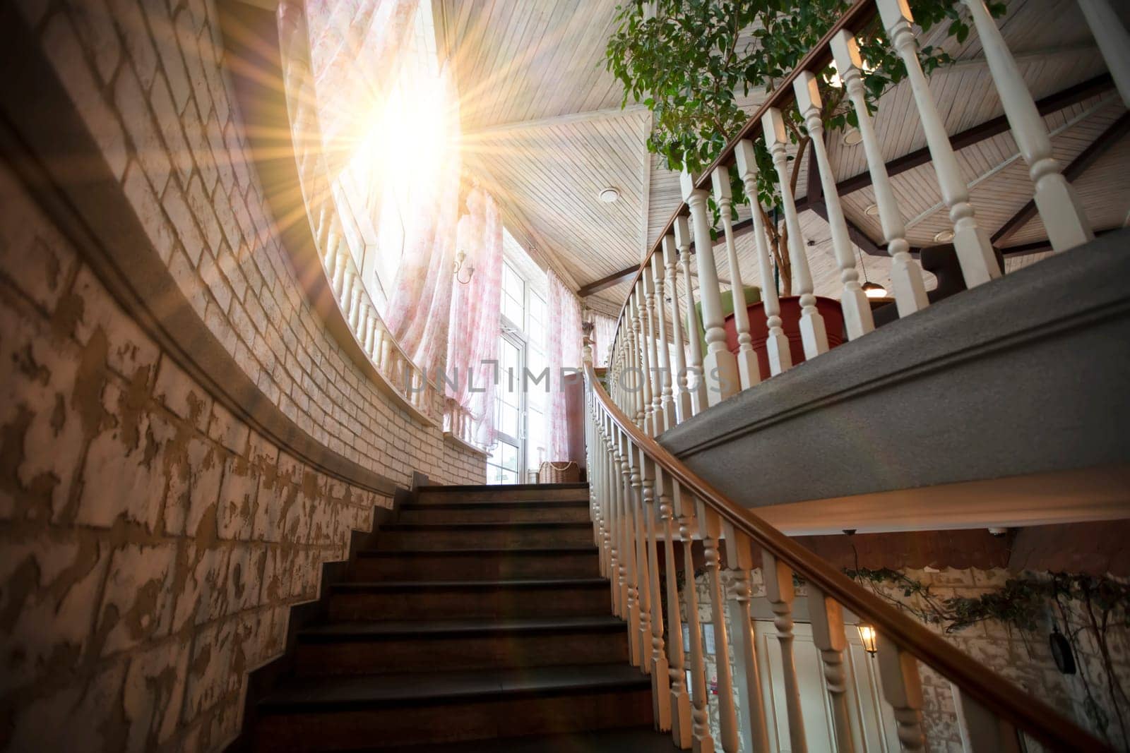 A spiral staircase with wooden railings leads up to the top illuminated by the sun.