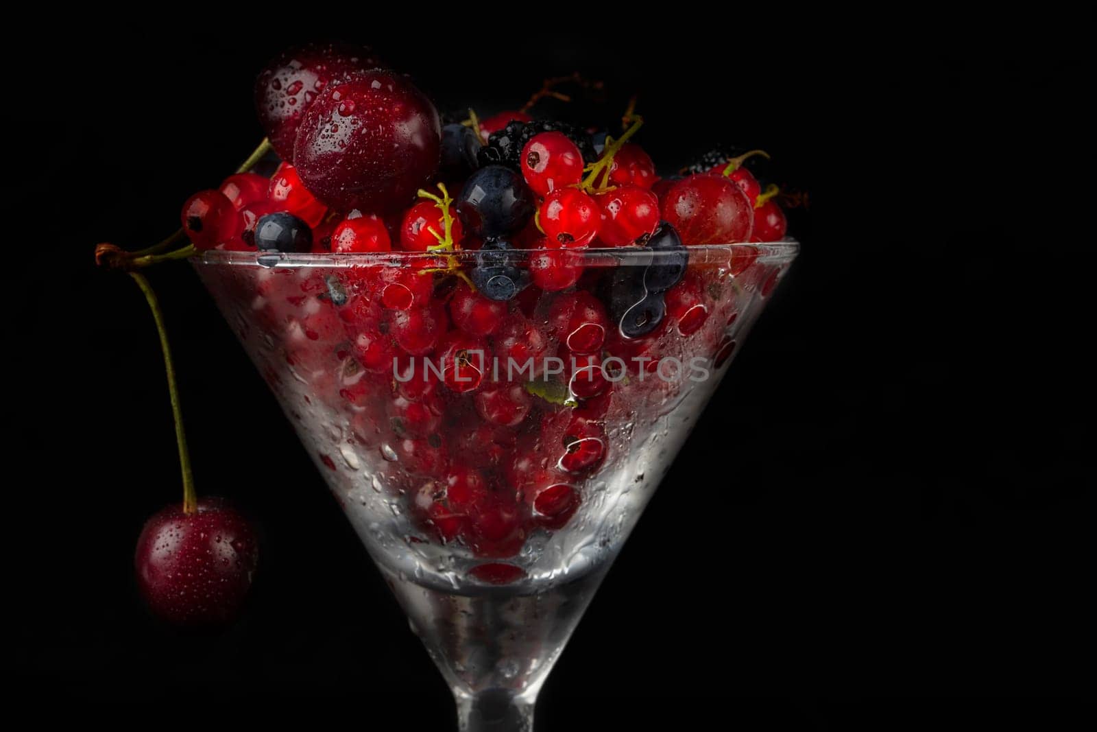 Summer berries in a glass glass on a dark background close-up.