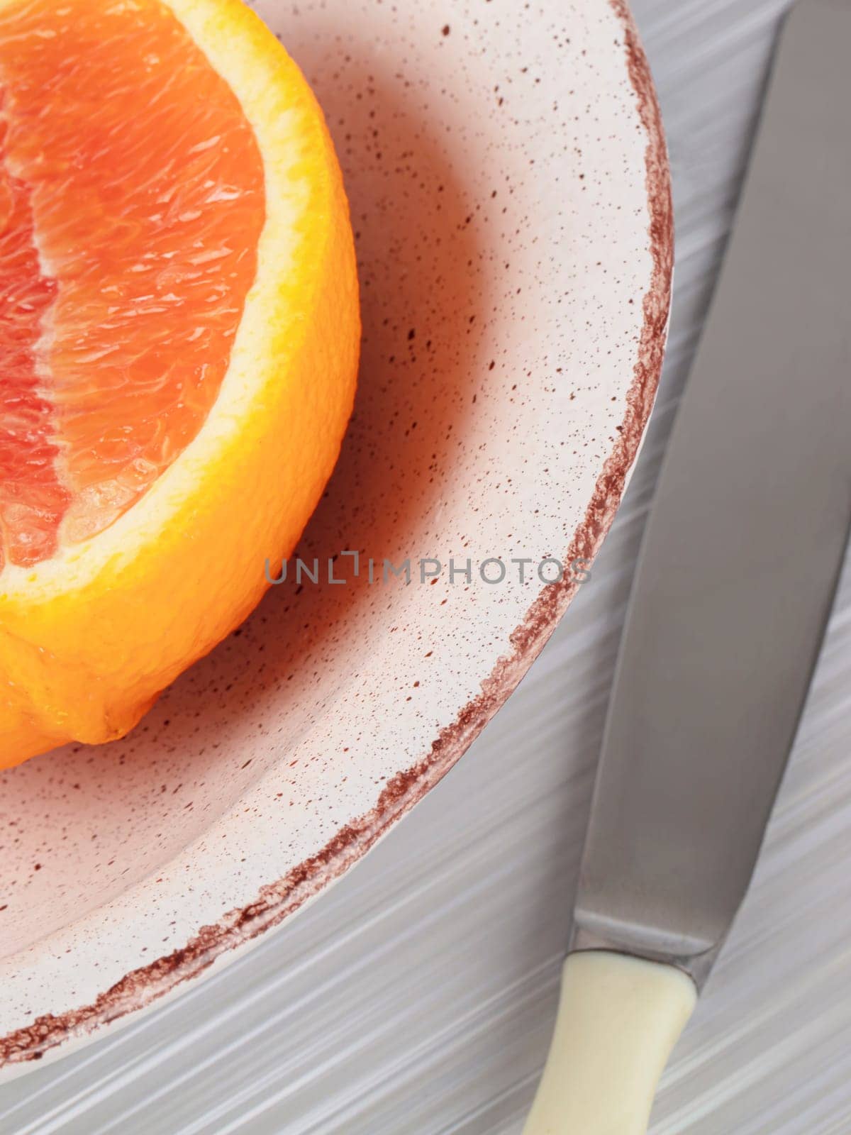 Part of a plate with half a grapefruit and a table knife. Photographed vertically.