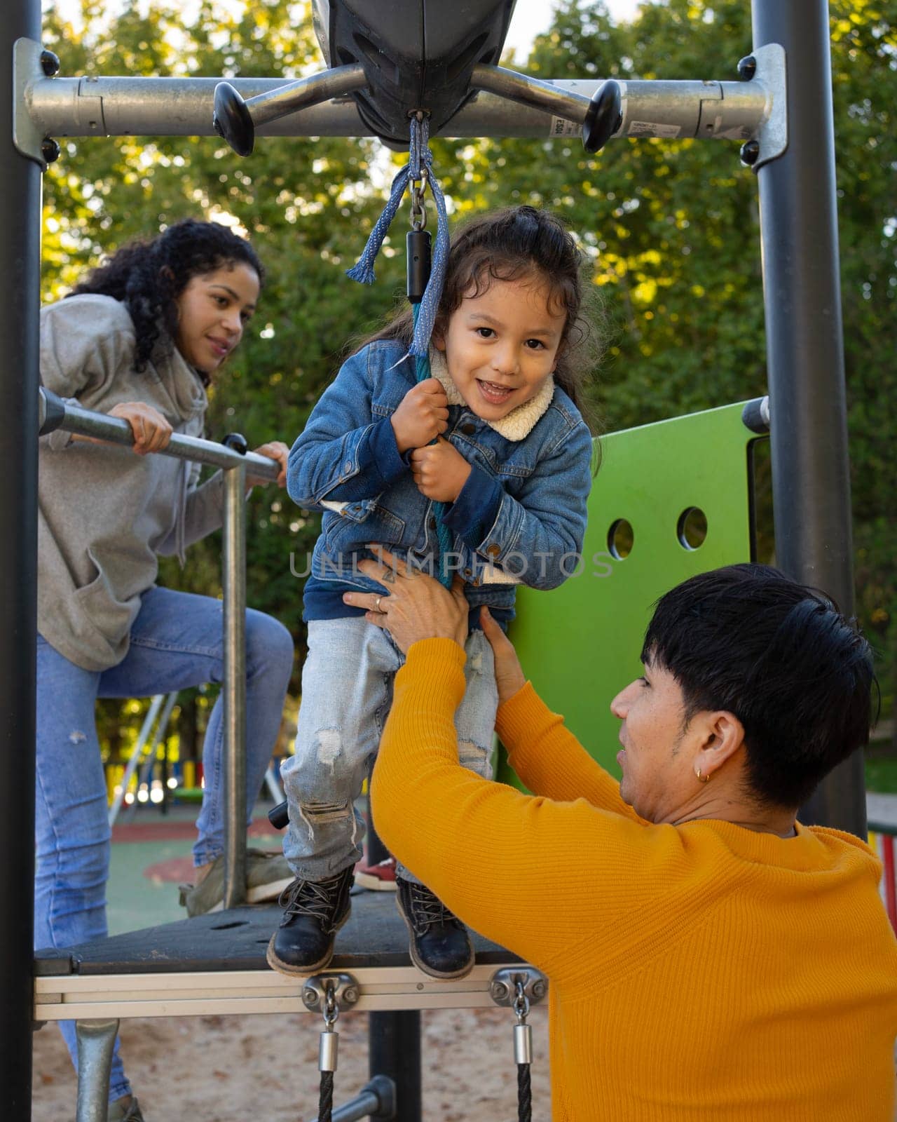 Latin family with a child playing in a playground. Father helping the kid to jump on a zipline.