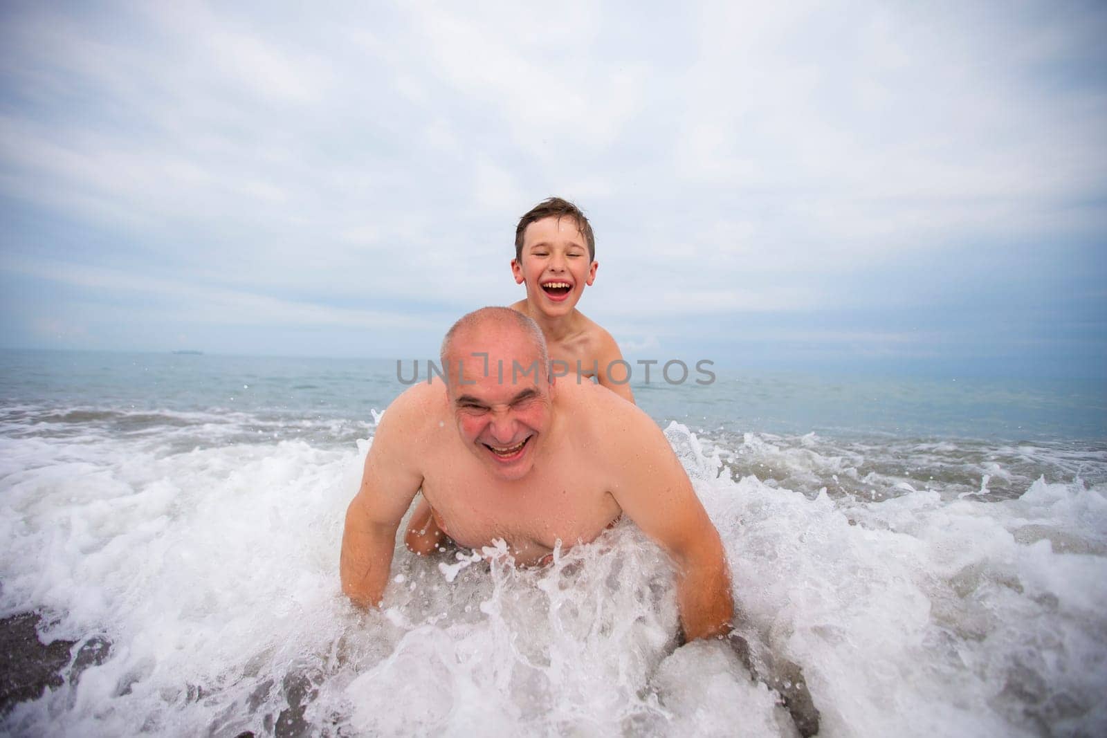 Happy boy swims and plays with grandpa on the beach. by Sviatlana