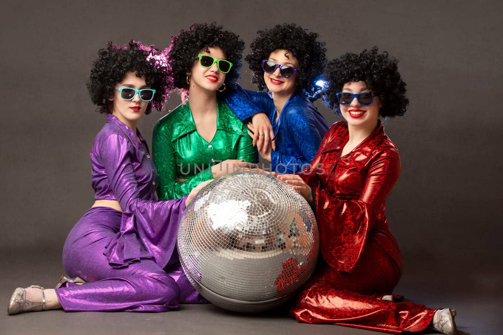 Group of happy girls in disco style, with disco ball, halloween party, on gray background. 80s themed party.