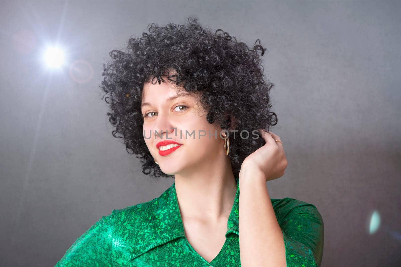 Excited woman in an afro wig on a gray background. Disco girl.