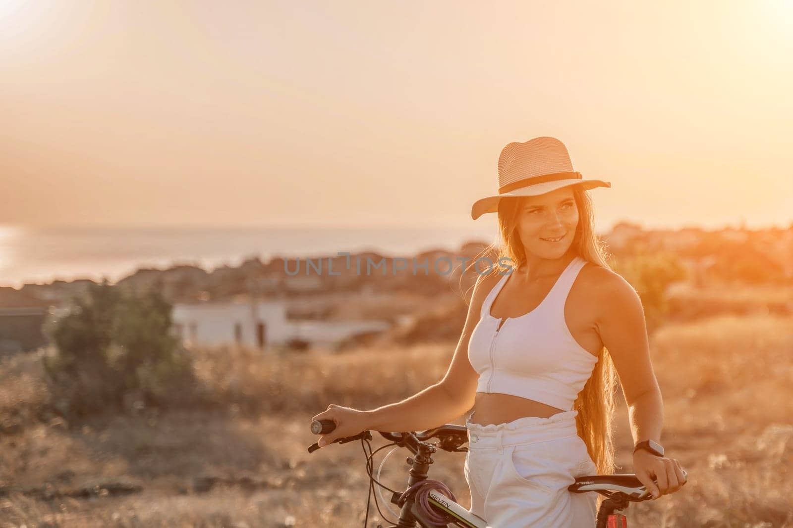 Woman travel bike. Happy woman cyclist sitting on her bike, enjoying the beautiful mountain and sea landscape, signifying the idea of an adventurous bike ride