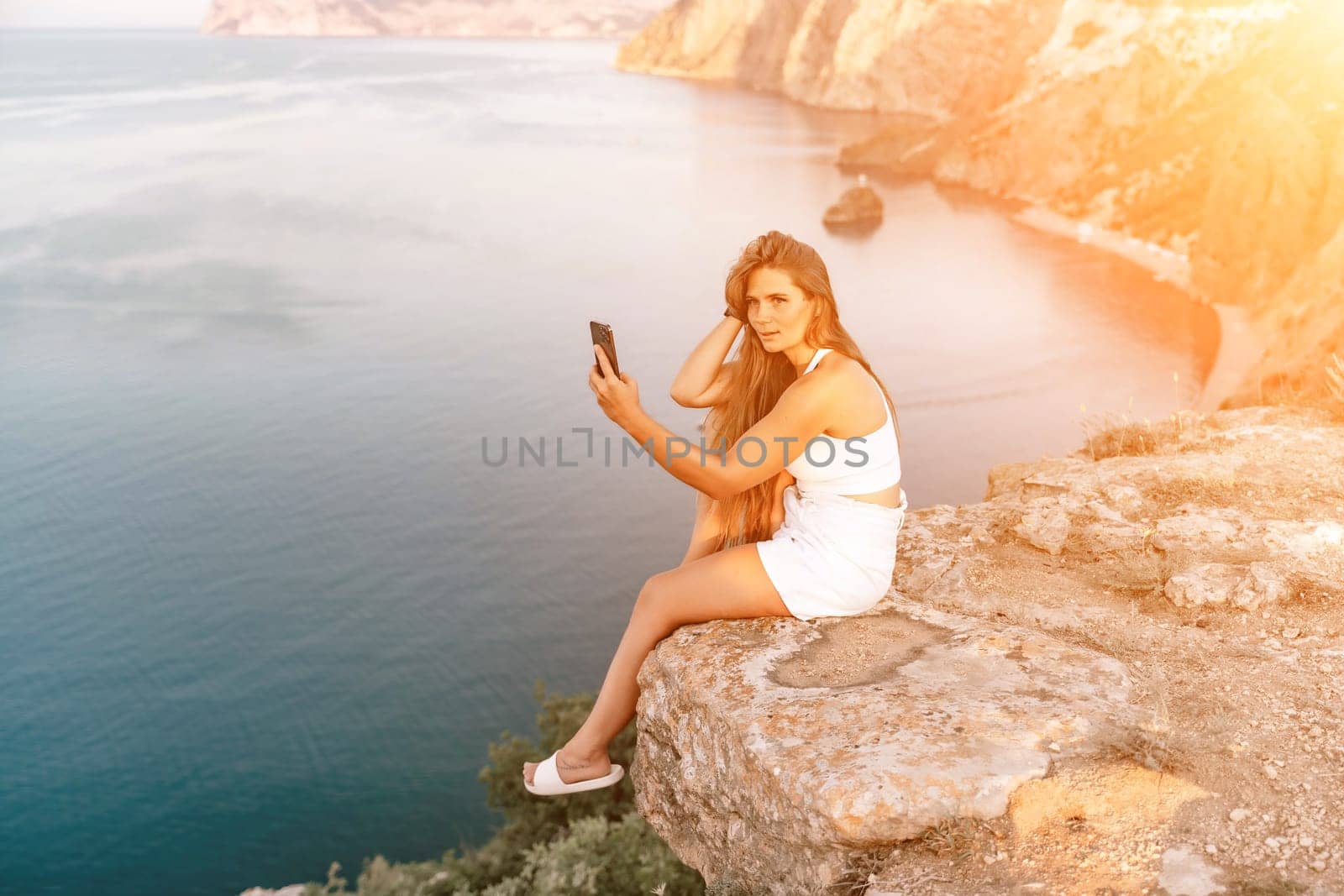 Selfie woman sea. white tank top, and shorts captures a selfie shot with her mobile phone against the backdrop of a serene beach and blue sea