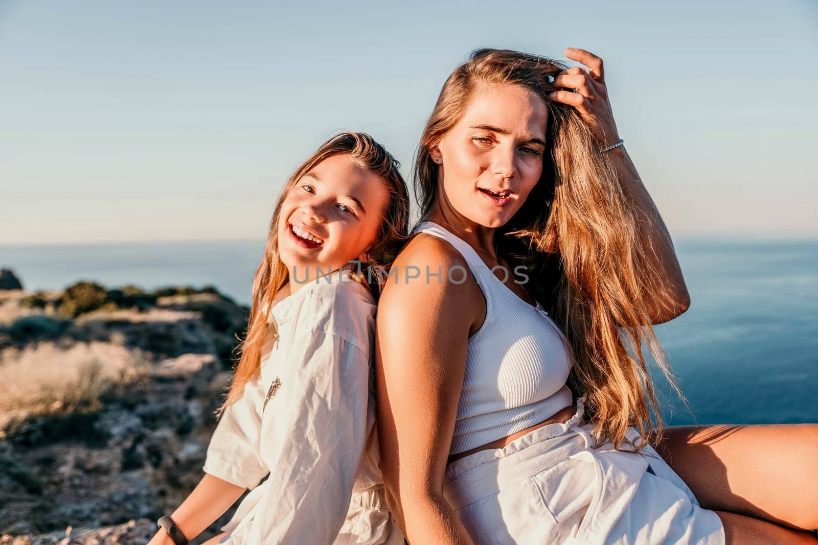 Sea family vacation together, happy mom and teenage daughter hugging and smiling together over sunset sea view. Beautiful woman with long hair relaxing with her child. Concept of happy friendly family. by panophotograph