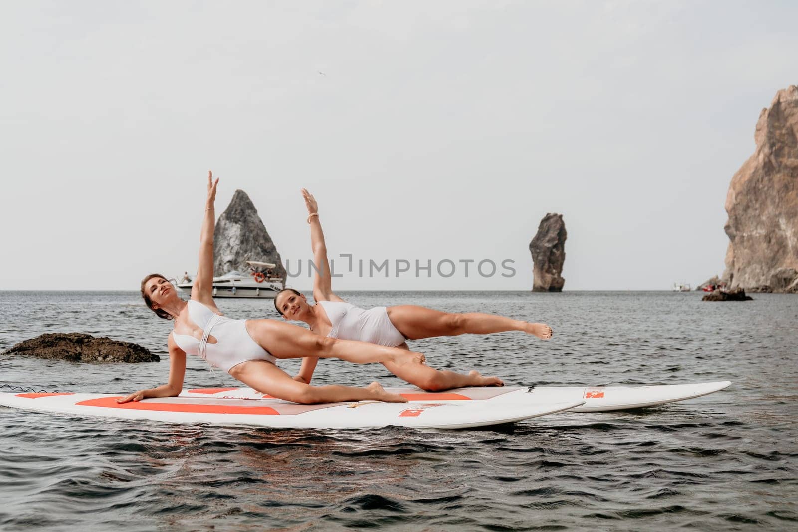 Woman sup yoga. Middle age sporty woman practising yoga pilates on paddle sup surfboard. Female stretching doing workout on sea water. Modern individual hipster outdoor summer sport activity