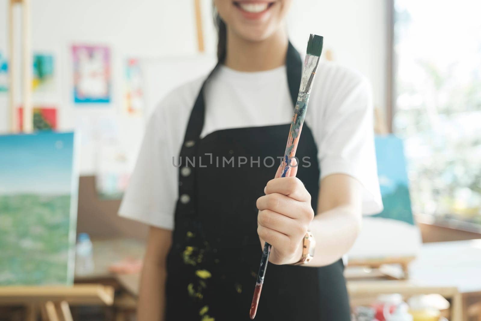 A close-up of the artist hands wearing an apron smeared with paint. Clutching many brushes and paintbrushes. Hobby and lifestyle concept.