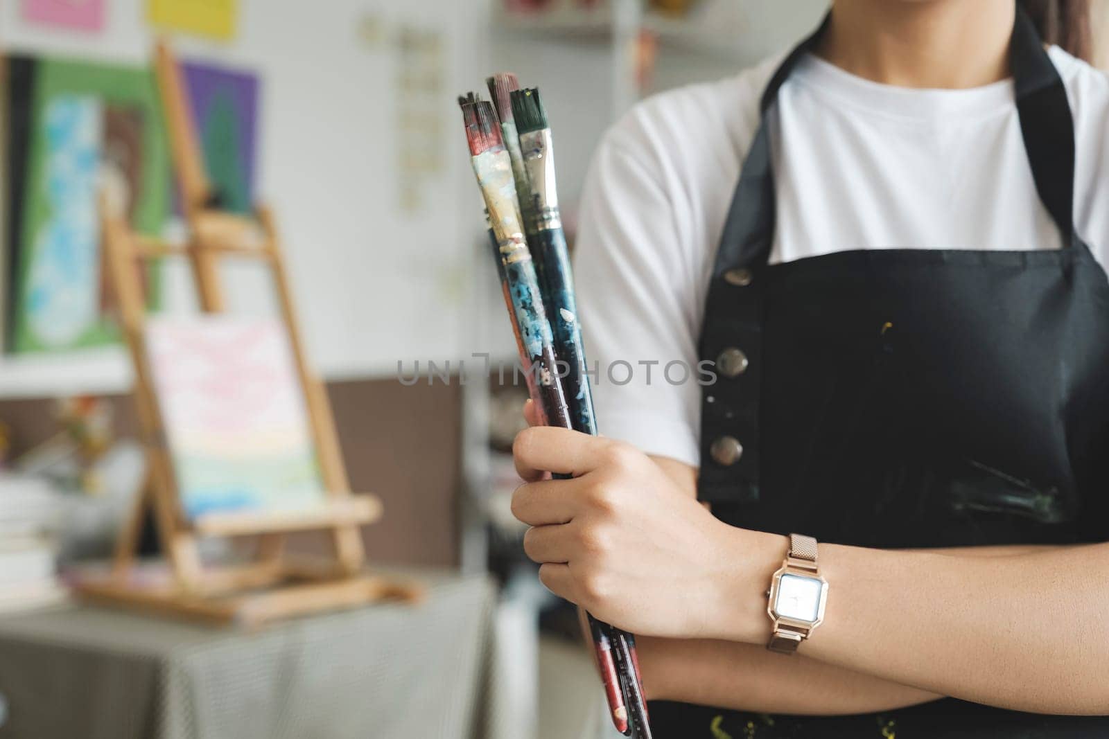 A close-up of the artist hands wearing an apron smeared with paint. Clutching many brushes and paintbrushes. by ijeab