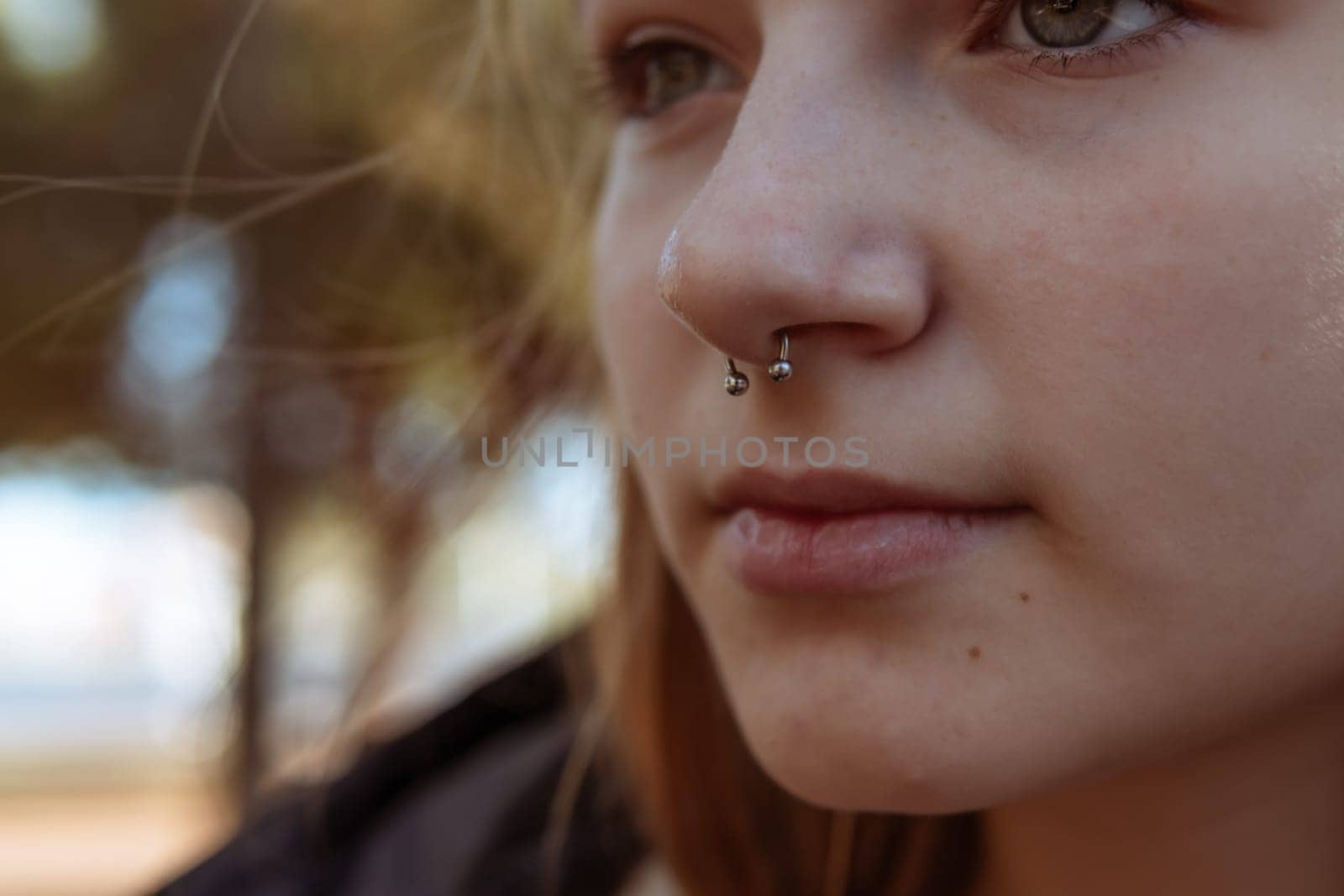 Young woman with a nose piercing against a blurred street background, close-up by PopOff