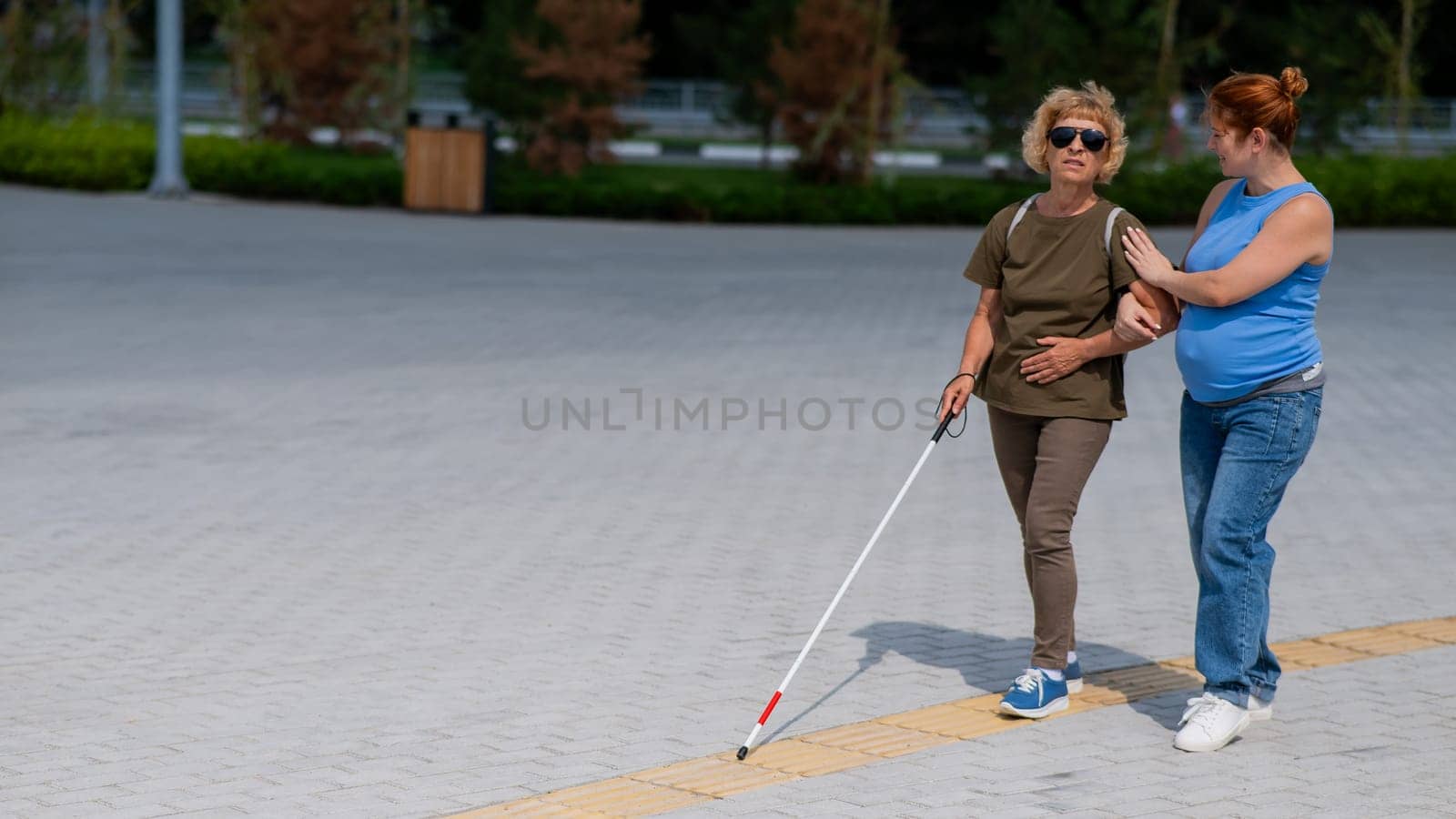 Caucasian pregnant woman leading blind elderly lady outdoors. by mrwed54