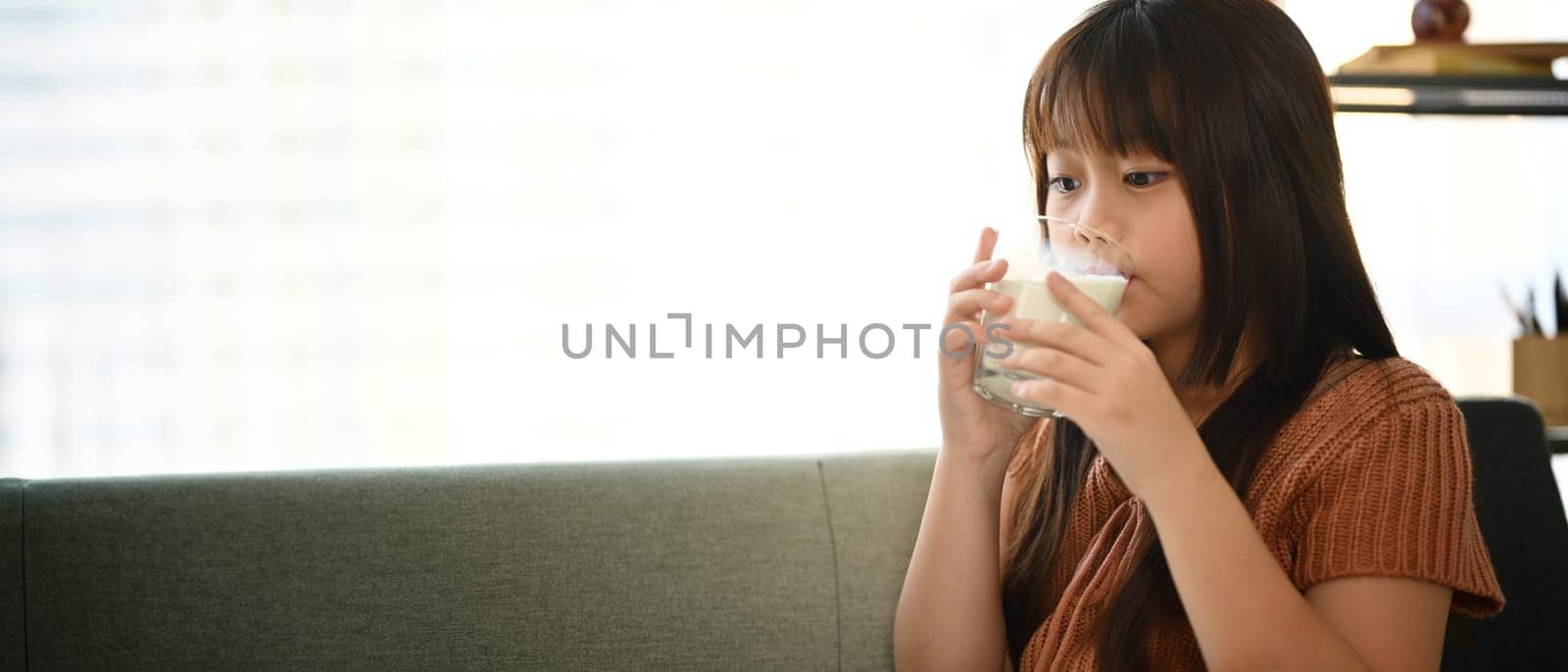 Cute little Asian girl in casual clothes drinking fresh milk. Growth and nutrition concept by prathanchorruangsak