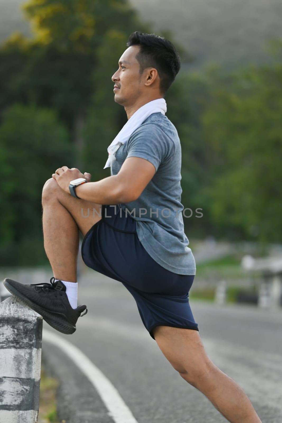 Portrait of motivated male athlete stretching legs before running in the park. Active lifestyle concept by prathanchorruangsak