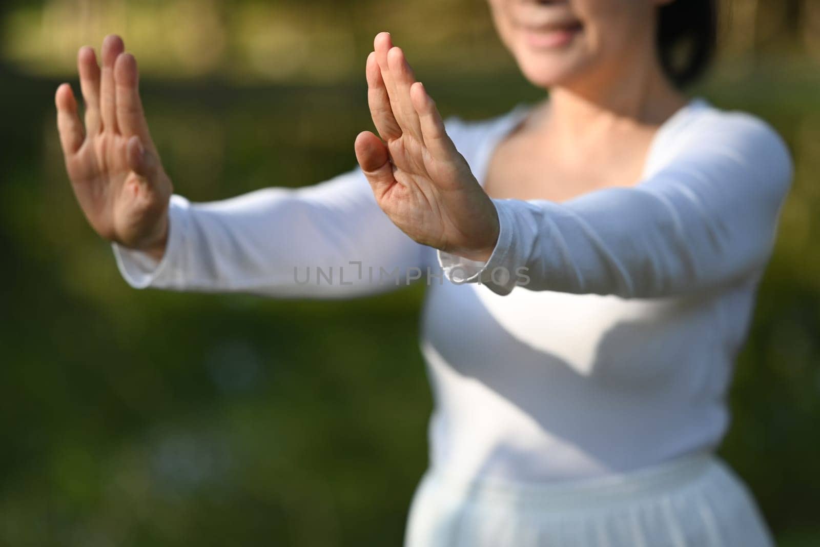 Smiling senior woman in white clothing practicing Tai Chi in the park. Health care concept.
