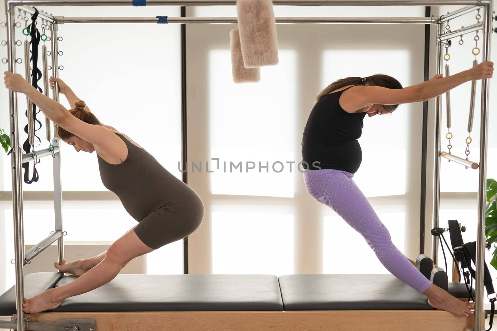 Two pregnant women are doing Pilates on a Cadillac reformer