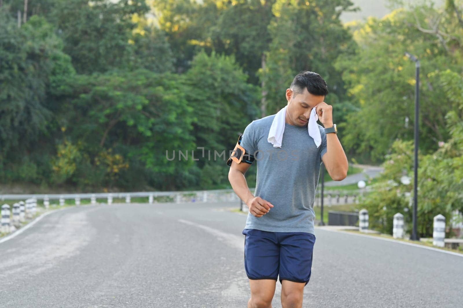 Shot of man runner wiping sweat with a towel while running in the city park.