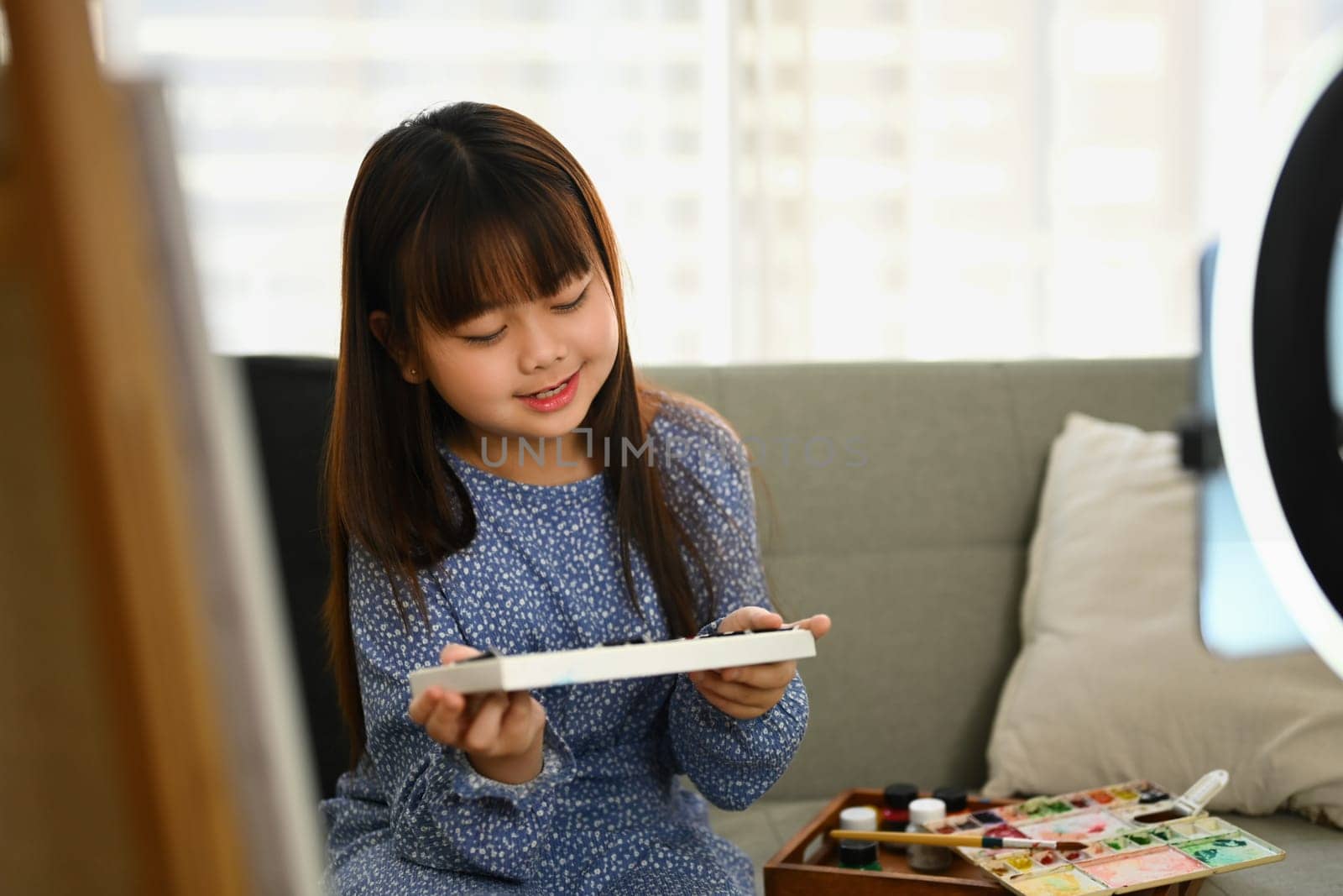 Pretty asian child girl painting picture at home and recording video for social media.