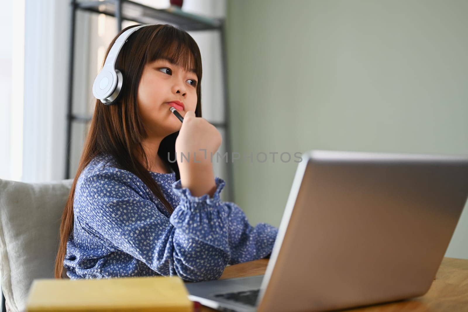 Image of Asian little cute girl with thoughtful face doing schoolwork at home.