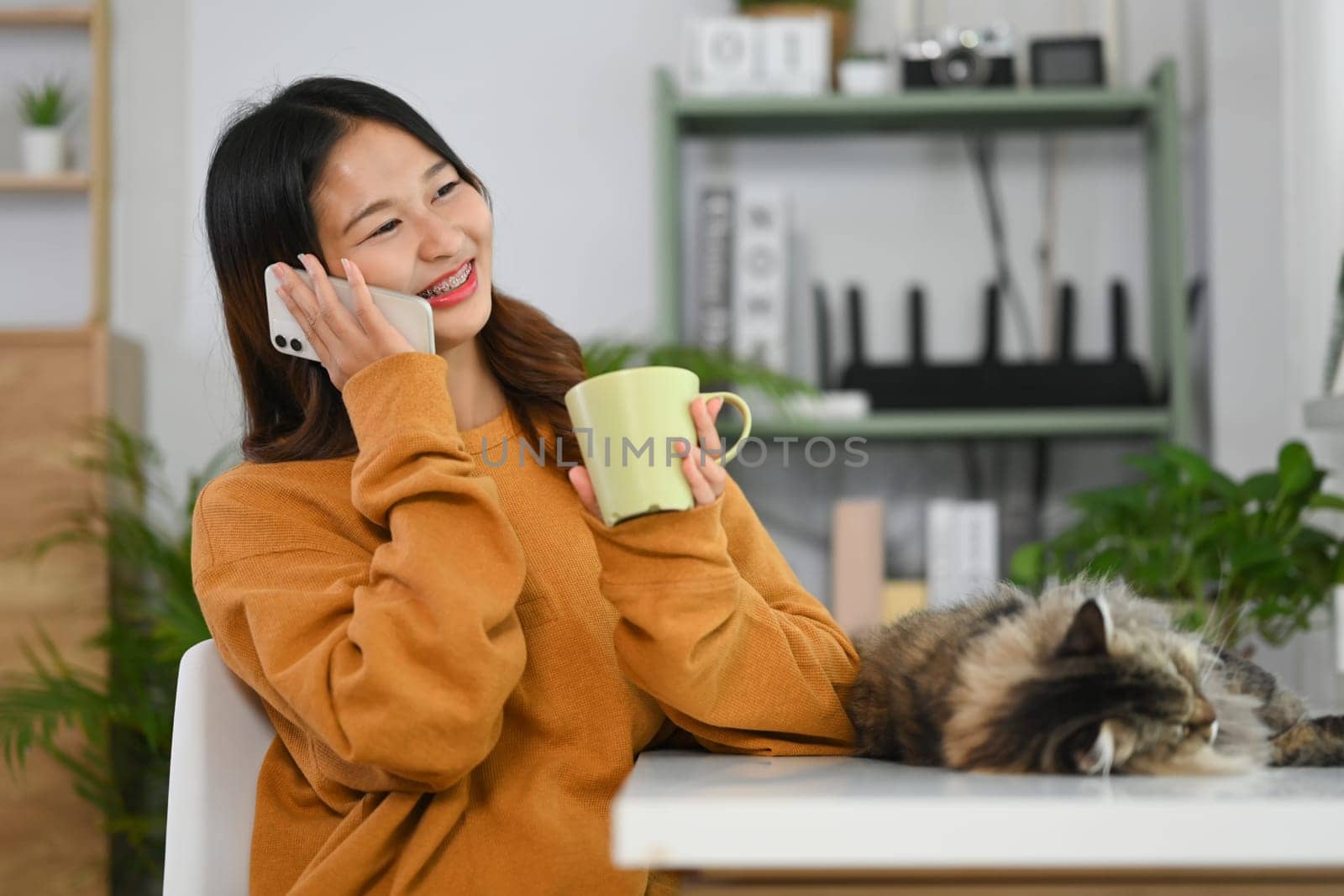 Pretty young Asian woman drinking hot tea and talking on mobile phone with friends or lover.