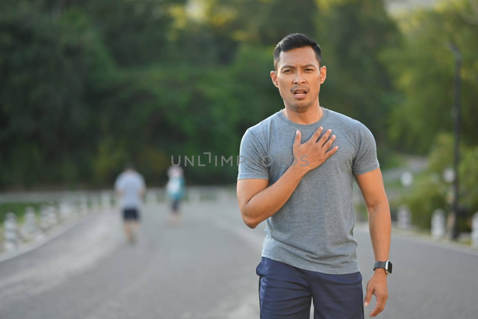 Tired sportsman touching his chest feeling pain in heart during exercise outdoor.