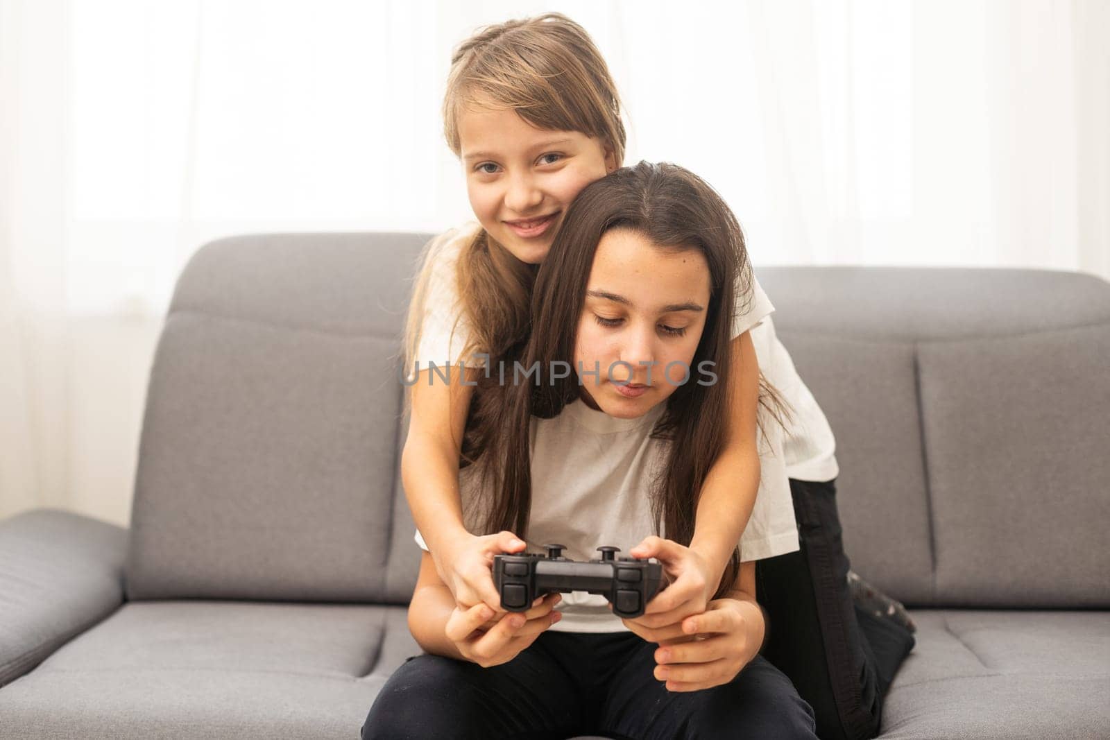 Two little girlfriends playing video game with joysticks. Excited and focused european children. Childhood concept. Entertainment and leisure. Idea of friendship. Grey background in studio. Copy space by Andelov13