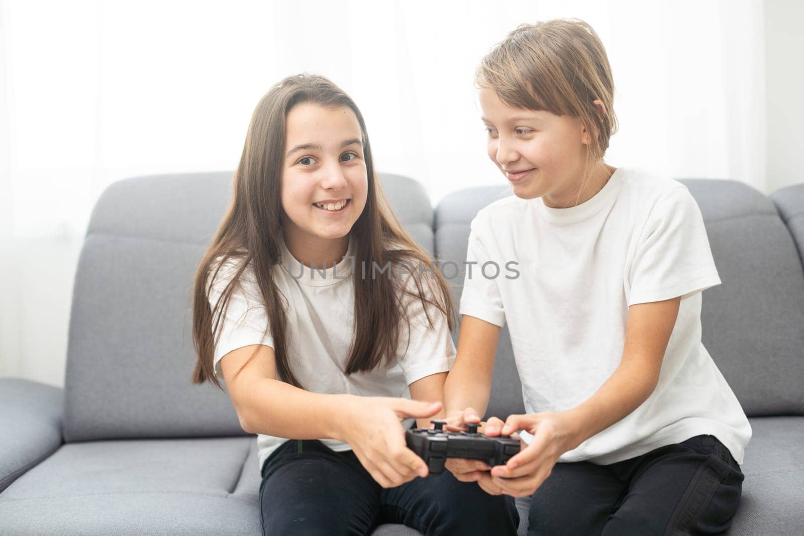Two sisters kids playing video games at home together. Happy childeren, carefree childhood concept. High quality photo