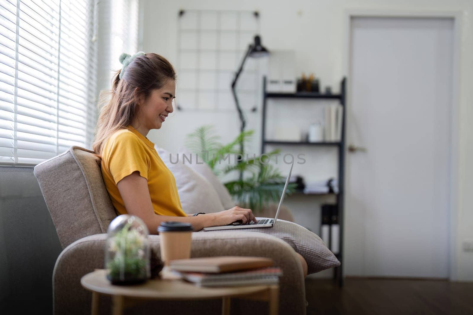 Young woman sitting on the couch and working on project, watching movie on laptop rest and happy chatting with friend in social network at home by nateemee