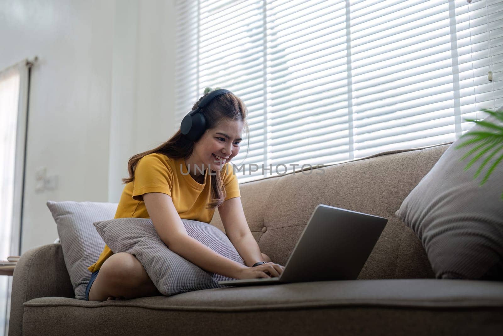 Happy woman wearing headphones watching and listening video on laptop and listening music sitting on a couch at home.