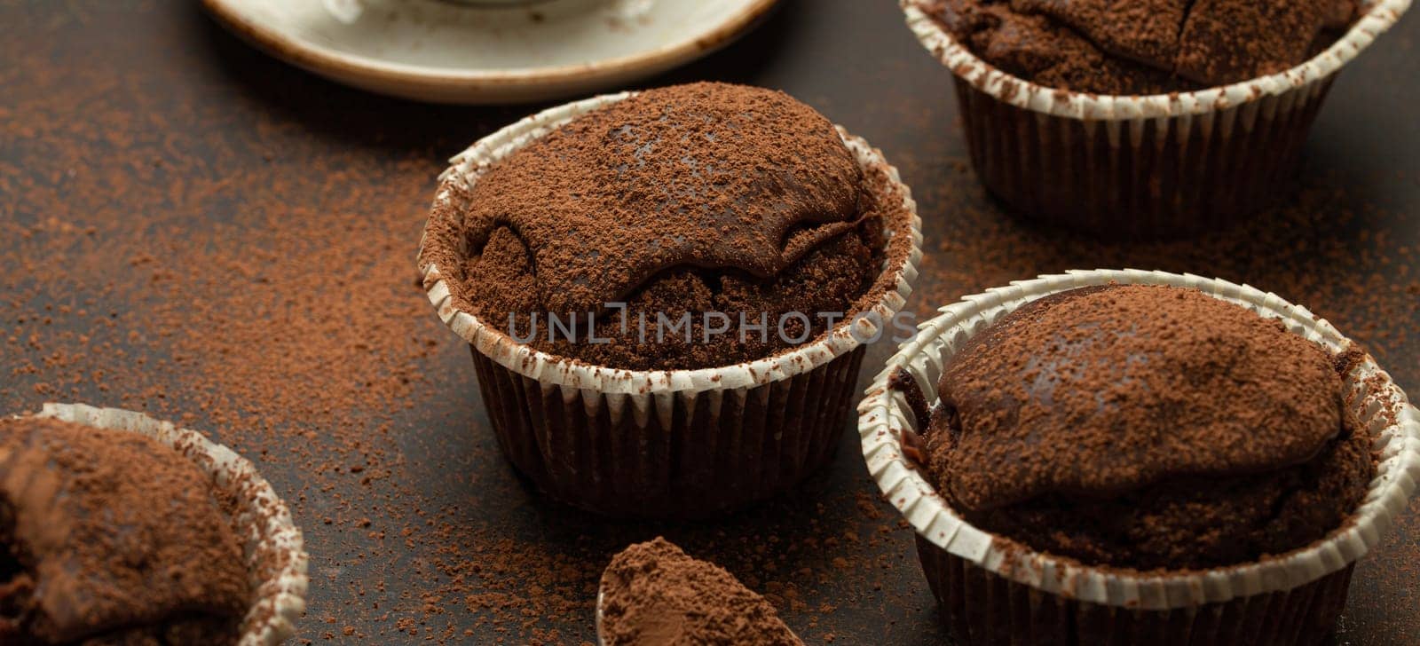 Chocolate and cocoa browny muffins with coffee cappuccino in cup angle view on brown rustic stone background, sweet homemade dark chocolate cupcakes.