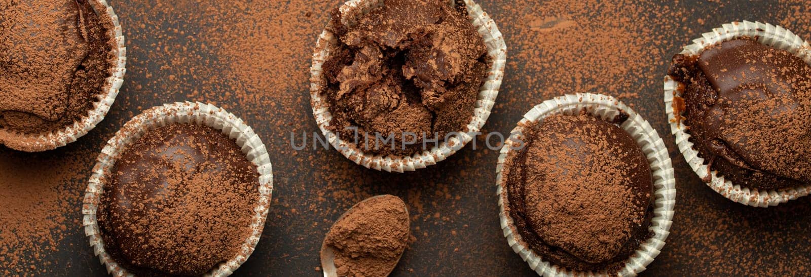 Chocolate browny muffins and cocoa in teaspoon top view on brown rustic stone background, sweet homemade dark chocolate cupcakes by its_al_dente