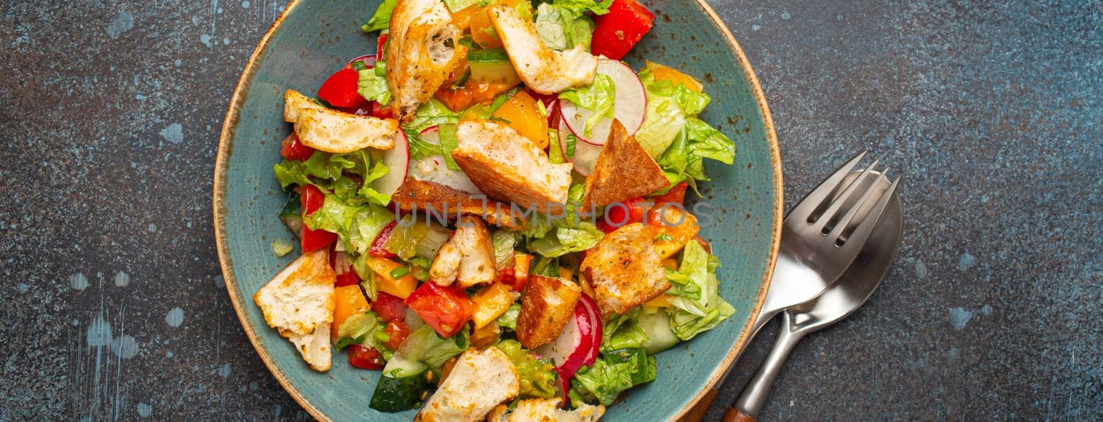 Traditional Levant dish Fattoush salad, Arab cuisine, made with pita bread croutons, vegetables and herbs. Healthy Middle Eastern vegetarian salad on plate, rustic dark blue background top view by its_al_dente