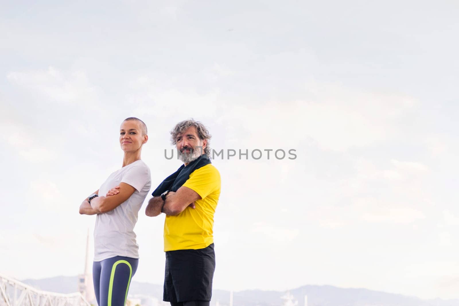 senior sportsman and young woman posing with arms crossed looking at camera, concept of active and healthy lifestyle in the middle age, copy space for text