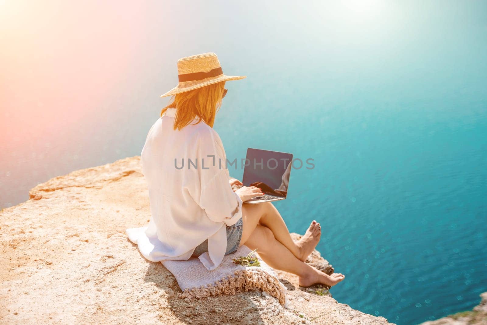 Freelance woman working on a laptop by the sea, typing away on the keyboard while enjoying the beautiful view, highlighting the idea of remote work