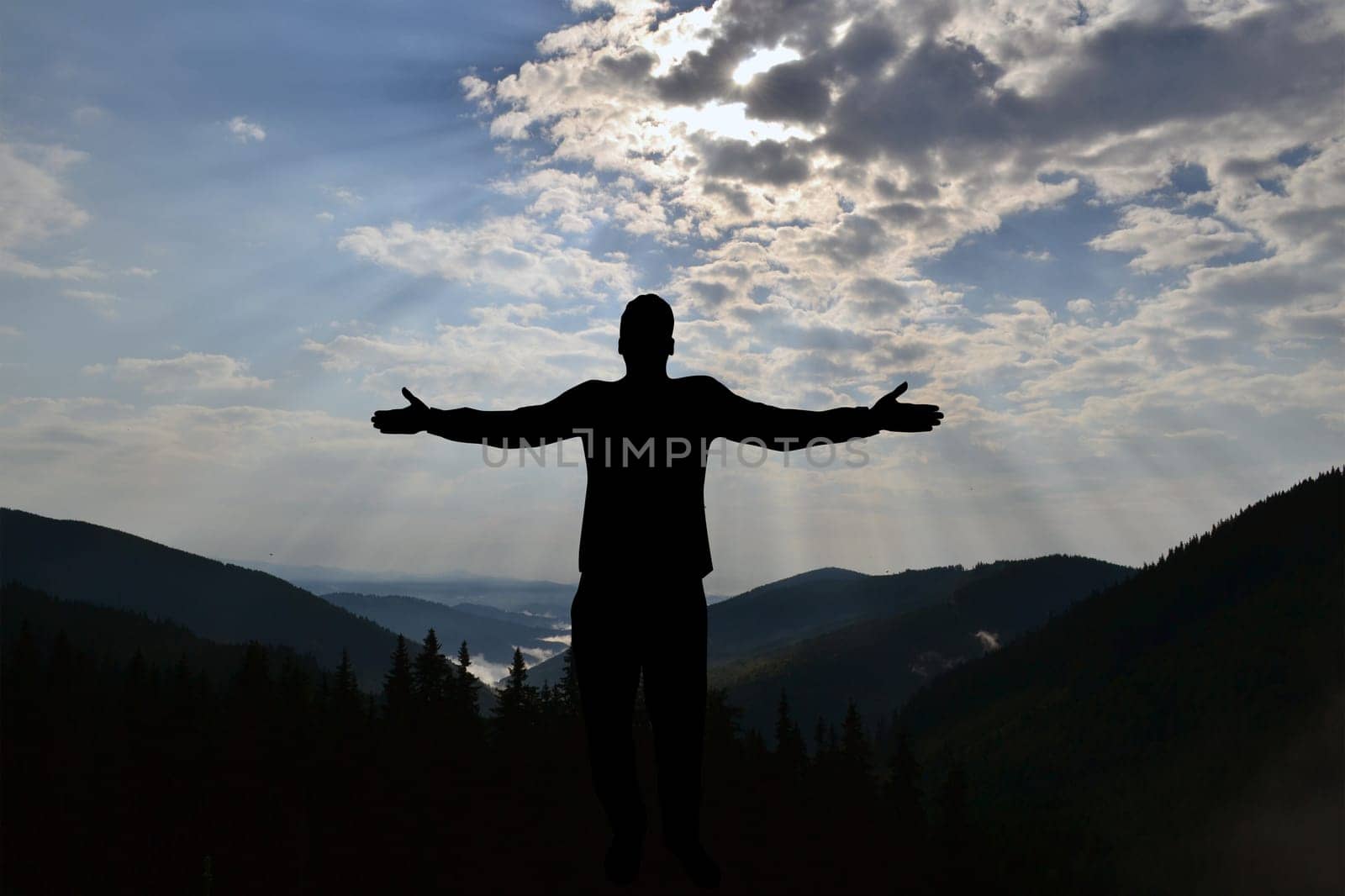 Silhouette of man enjoying freedom with open hands on mountains