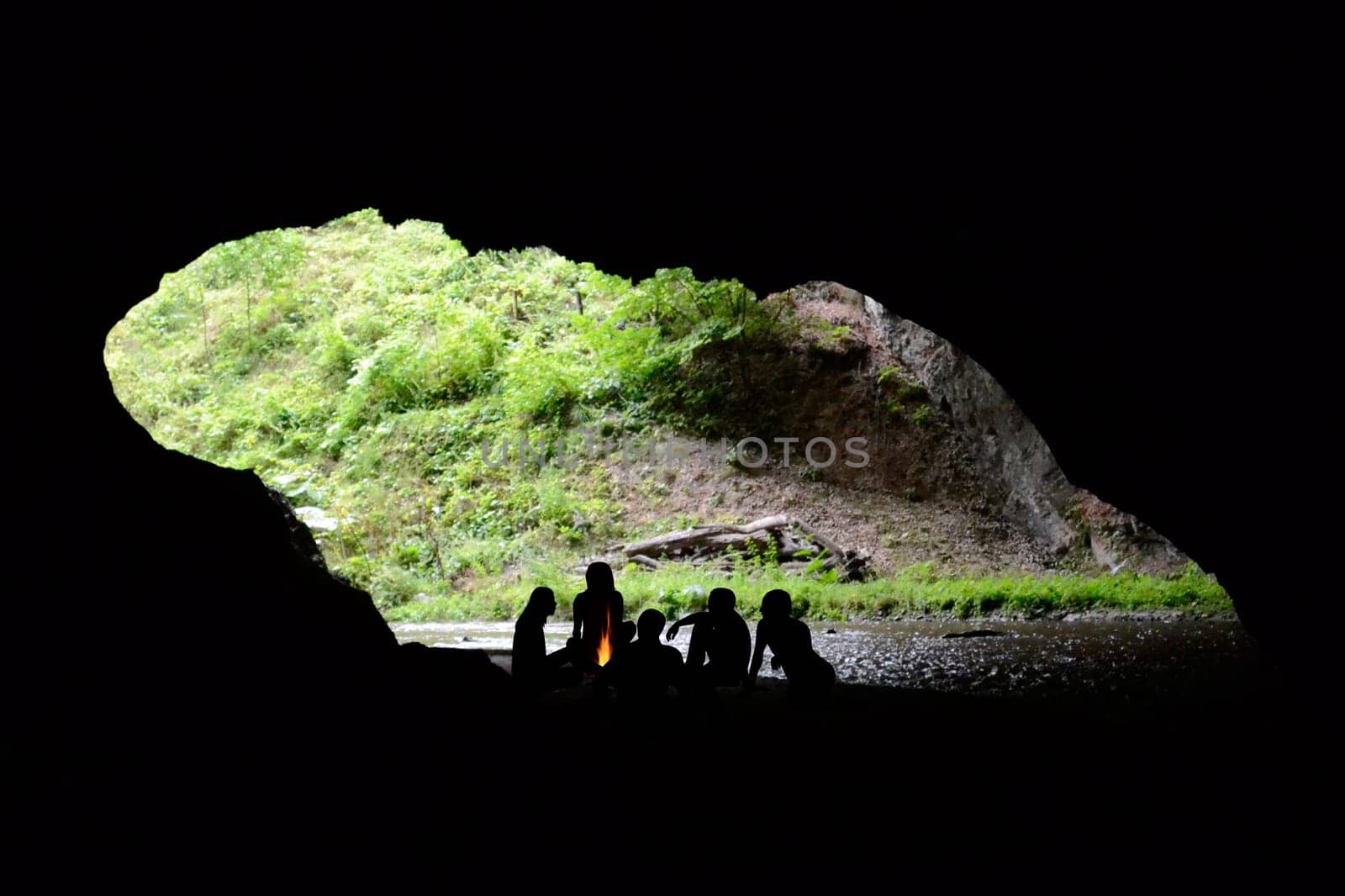 People silhouettes sitting around the fire in a cave