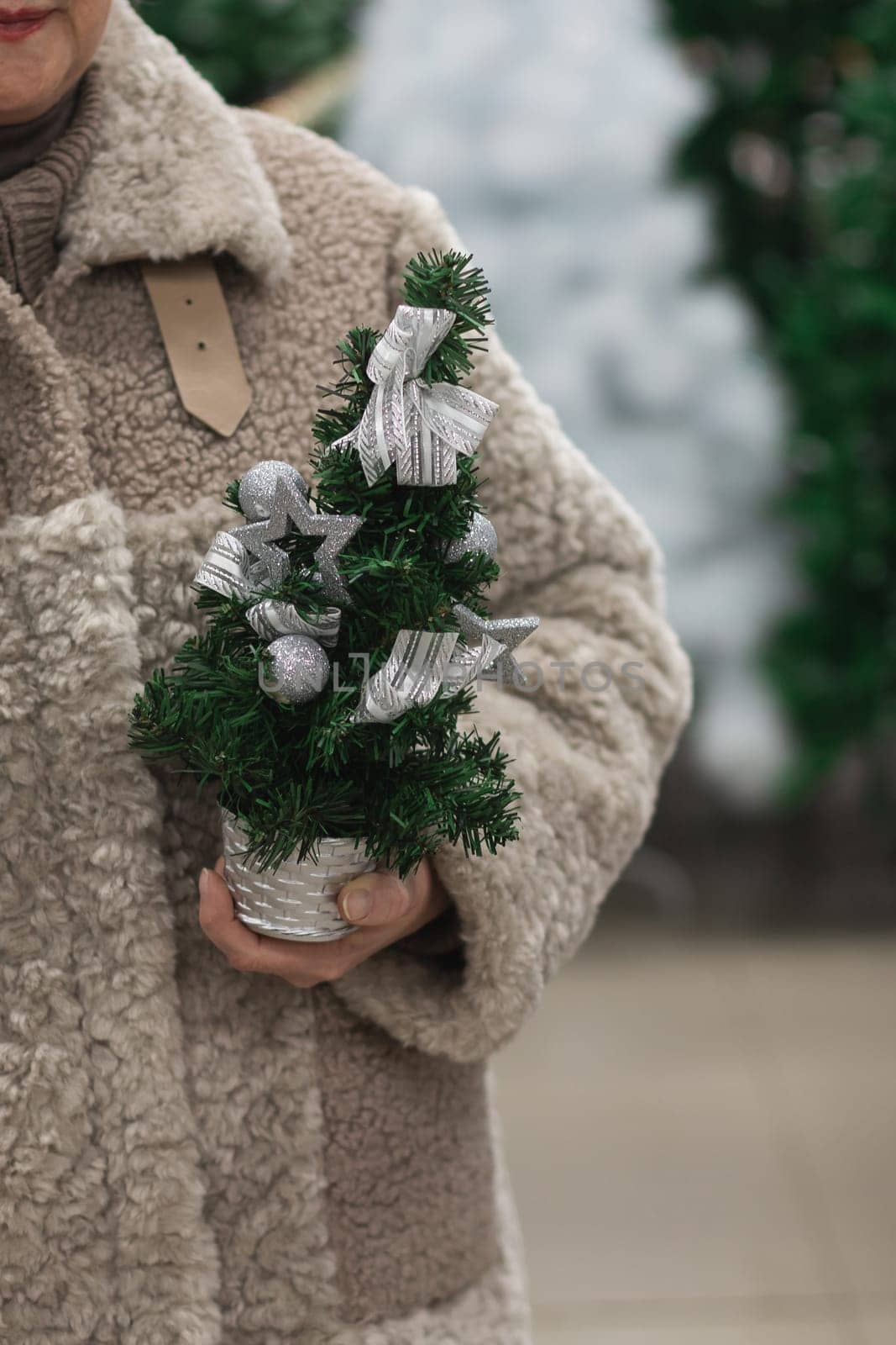 A woman in a fur coat holds a small artificial Christmas tree in her hands
