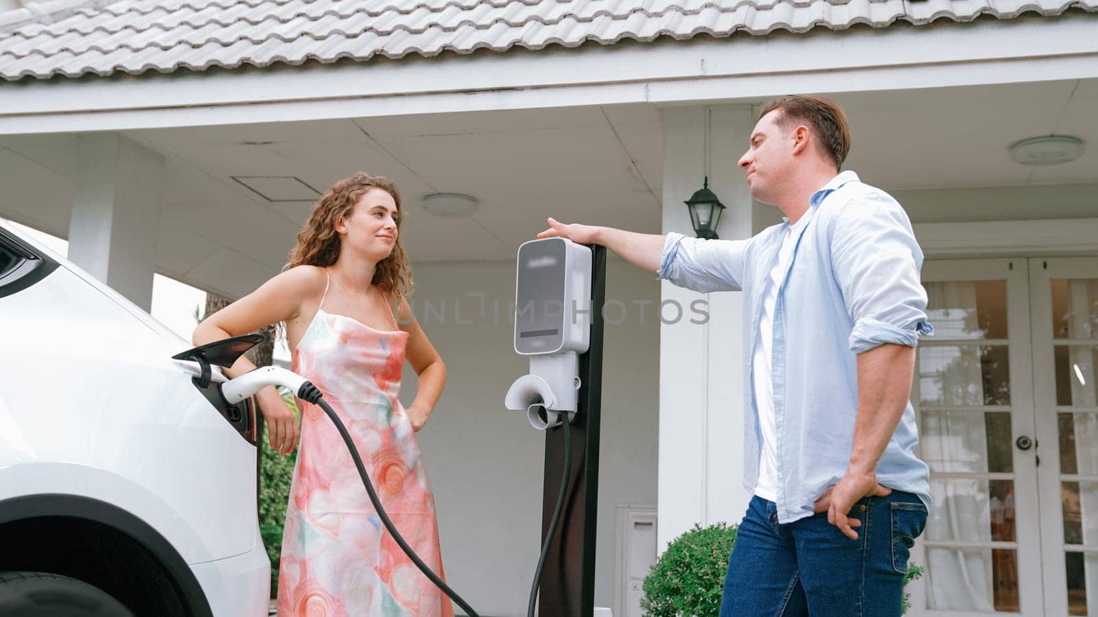 Happy and lovely couple with eco-friendly conscious recharging electric vehicle from EV charging station. EV car technology utilized as alternative transportation for future sustainability. Synchronos