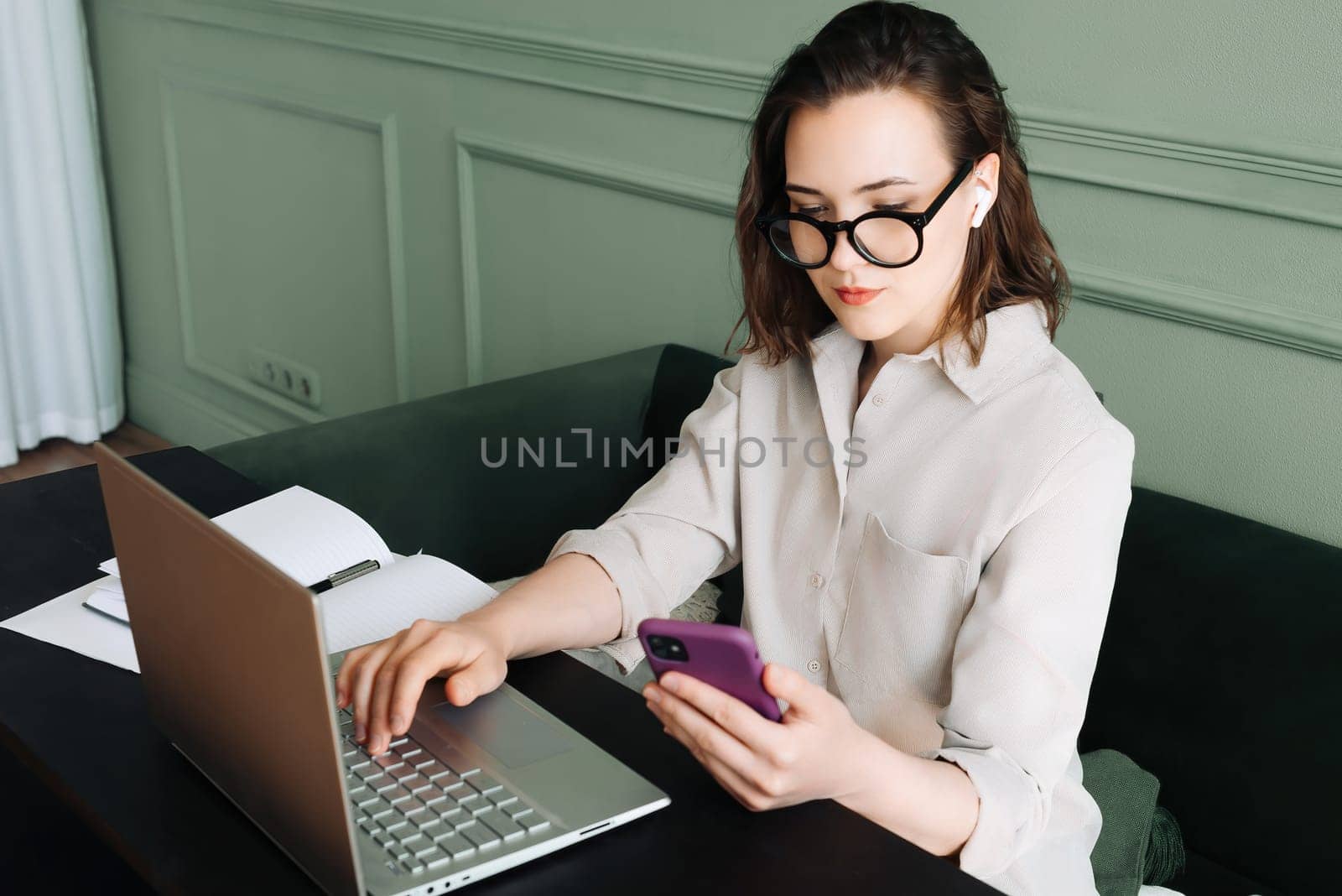 Productive Conversations. Woman Balancing Laptop and Smartphone in Video Call. Multitasking Joy. Busy Woman in Glasses Juggles Video Call on Laptop and Smartphone with a Smile.