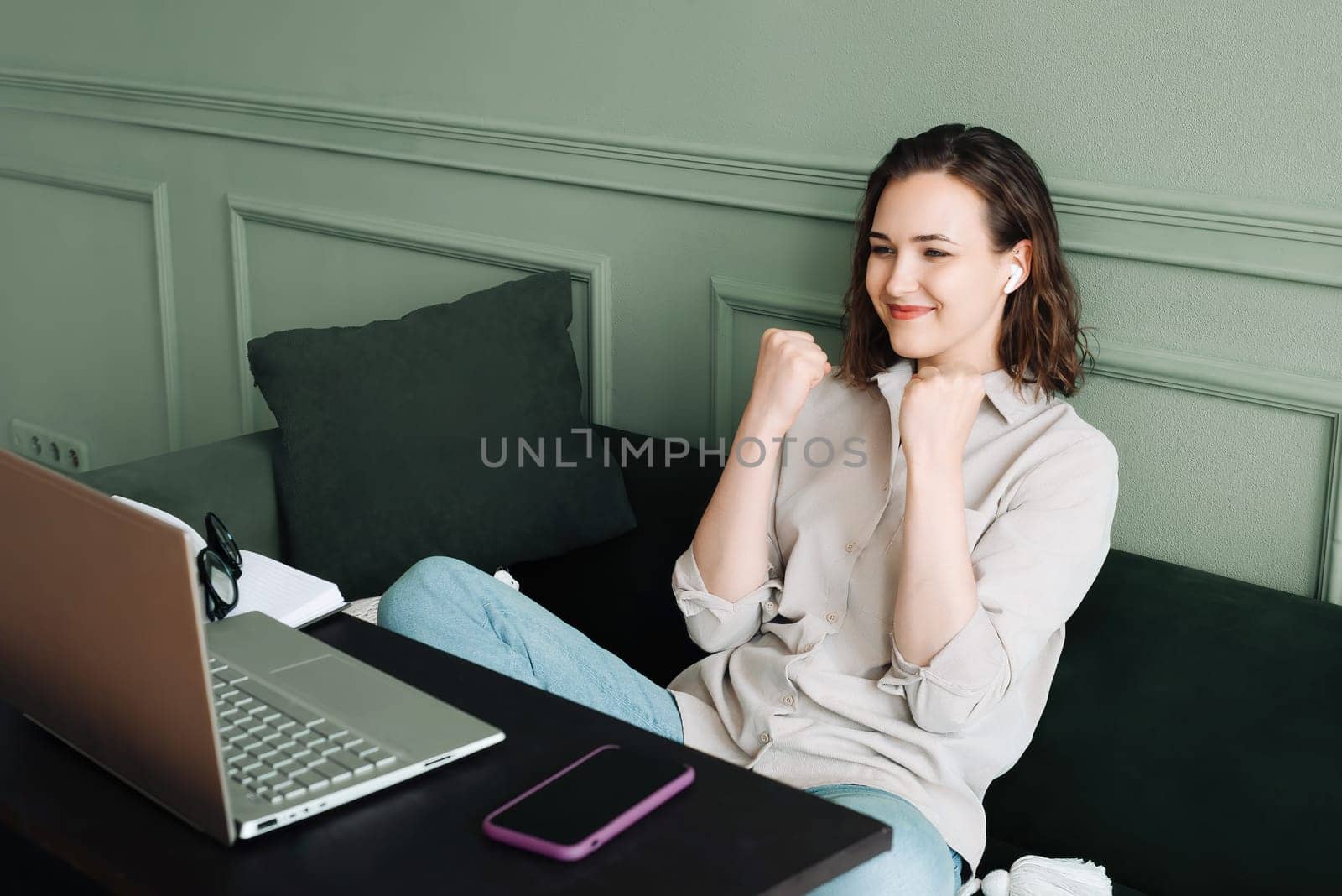 Winning and celebrating. Smiling woman gesturing in a successful video chat on her laptop. Happy woman in glasses is beaming as she communicates on her laptop, signalling victory and success