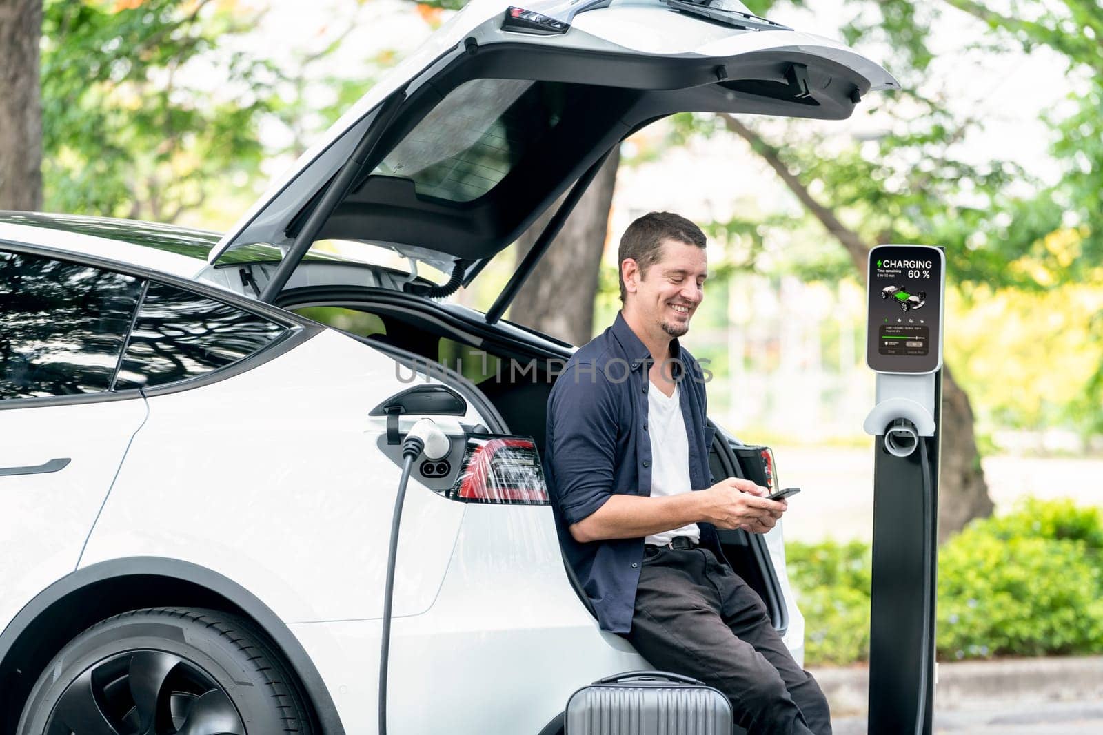 Man using smartphone online banking application to pay for electric car battery charging from EV charging station during vacation holiday road trip at national park or summer forest. Exalt