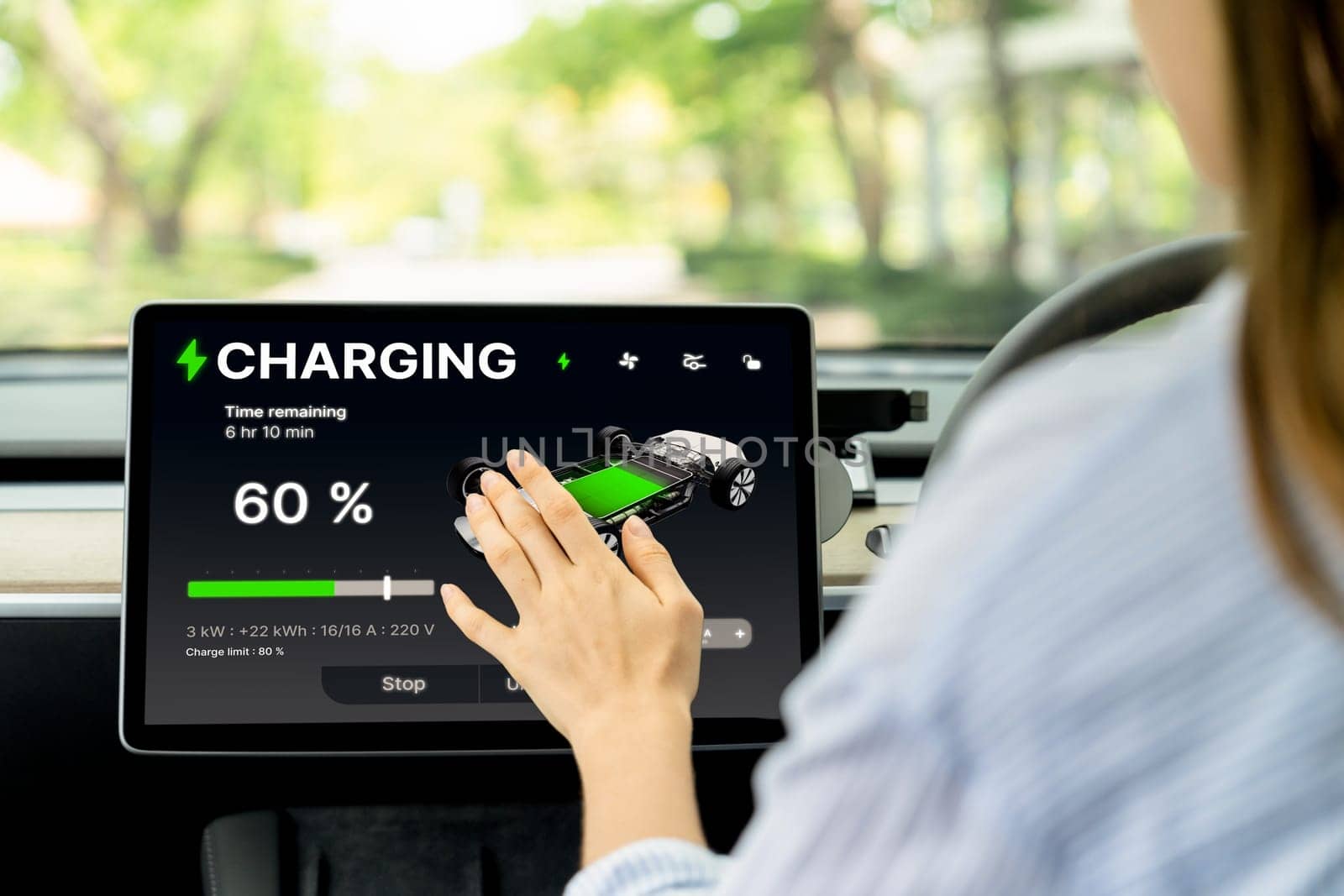 Young woman inside the vehicle, checking EV vehicle's application on battery recharging electricity status display on smart monitor screen in modern EV car on her road trip journey. Exalt