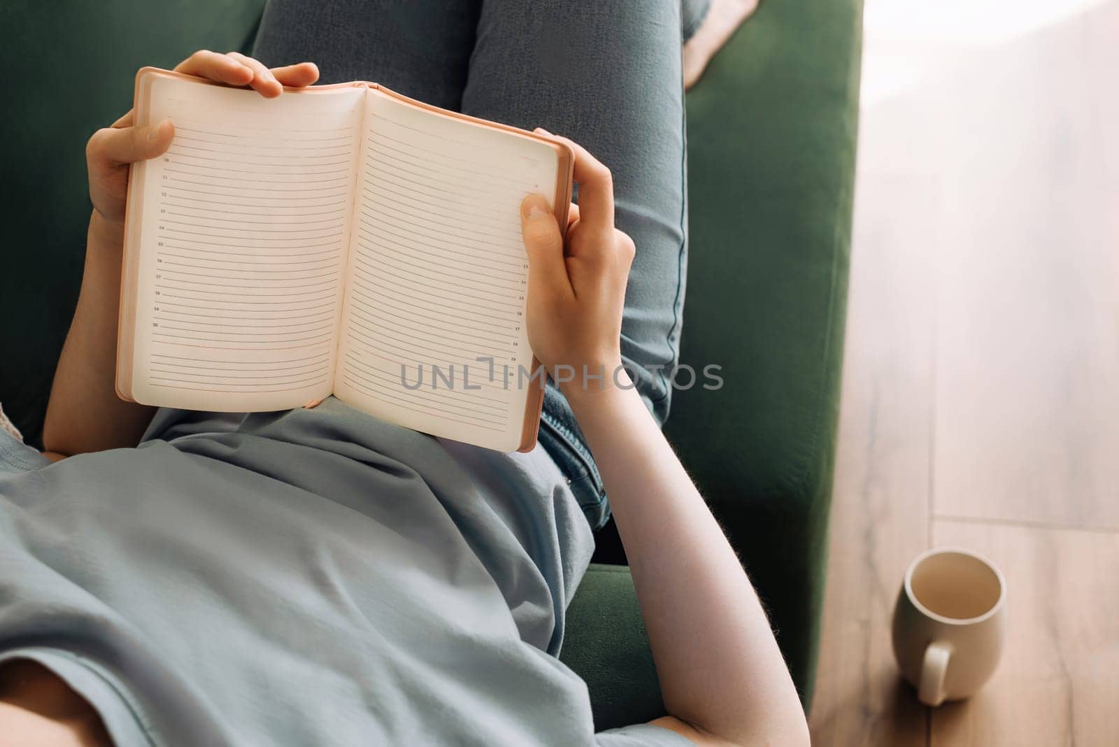 Relaxed Young Woman Enjoying Book, Tea on Living Room Sofa. Cozy Leisure Time. Lady Reading, Sipping Tea in Comfortable Home Setting. Relaxation and Gastronomic Pleasure in Domestic Atmosphere.