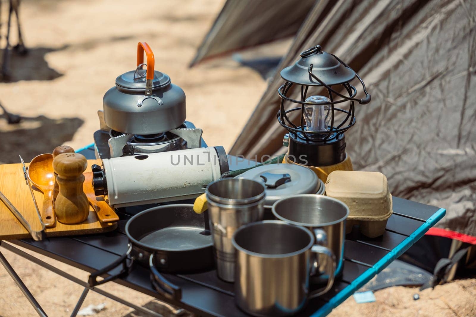 A picturesque morning at the campsite, essential cooking equipment, kettle, pot, pan, gas stove, and camera, set up by the tent. Camping in nature has never been more delightful. by Sorapop