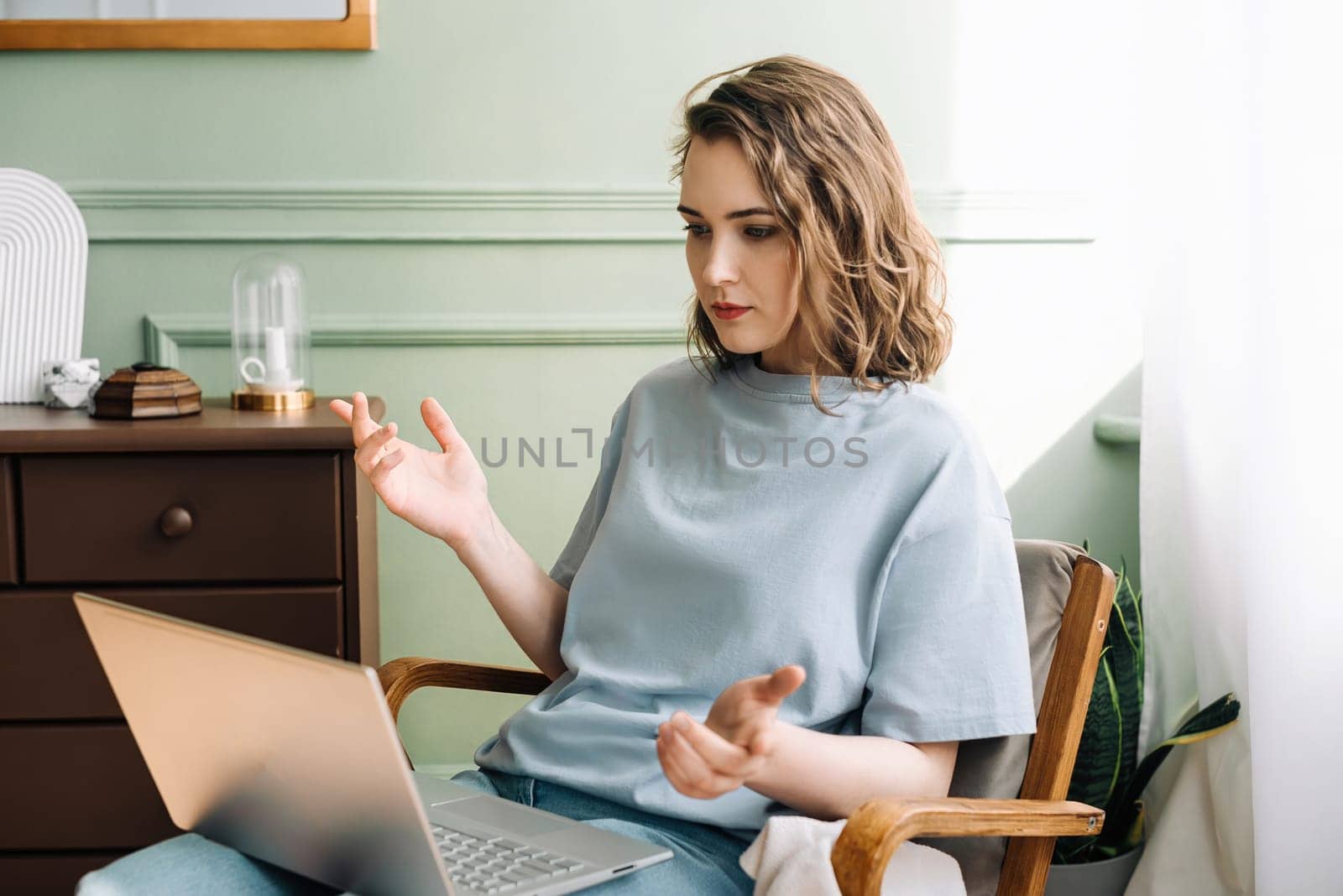 A serious woman works at her laptop, discovering a bug, has a video call in the living room. Problem-Solving Pro. Serious Woman on Laptop with Bug Discovery During Video Call.