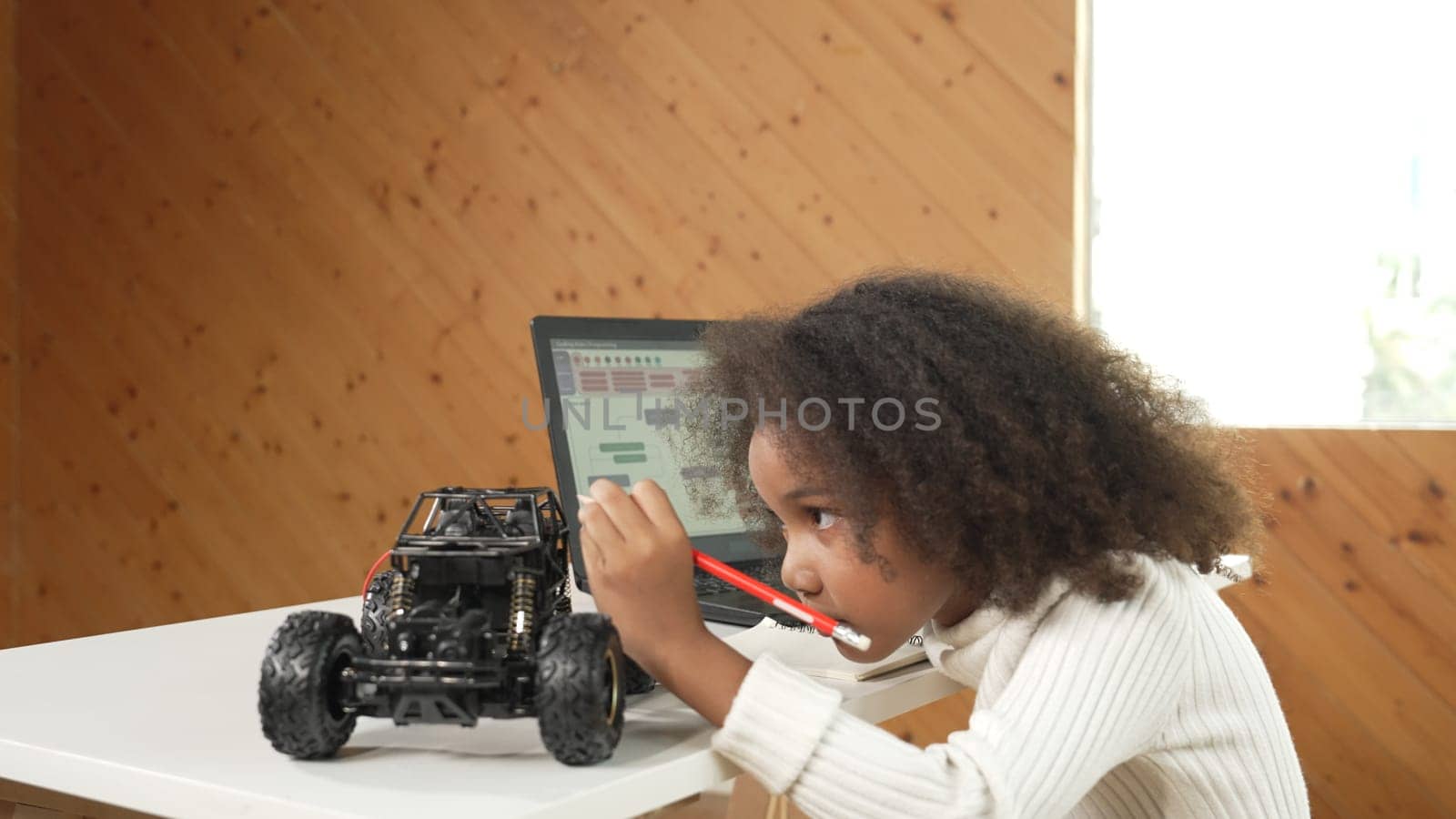 African girl pointing at car model structure while work on laptop. Student inspect at STEM education class. Panorama shot of Clever child using laptop to write programing engineer code. Erudition.