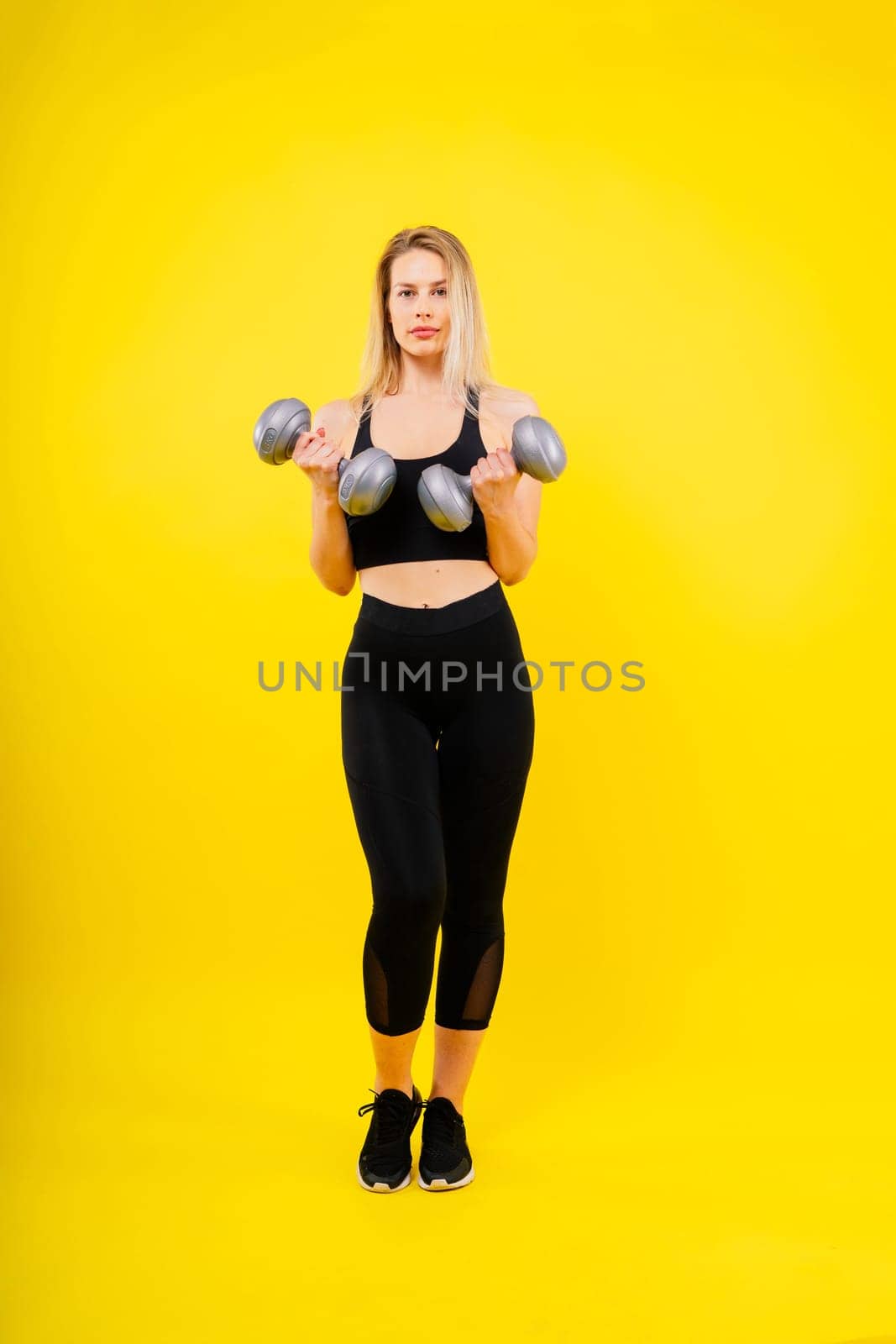 Athletic woman in sportswear raises dumbbells leads healthy lifestyle has happy expression by Zelenin